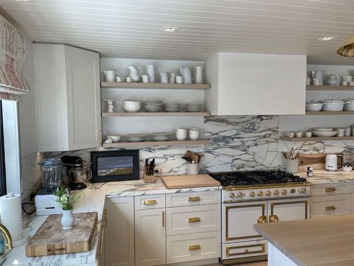 Bright white kitchen with marble backsplash, open shelves, and a stove centered under a hood.