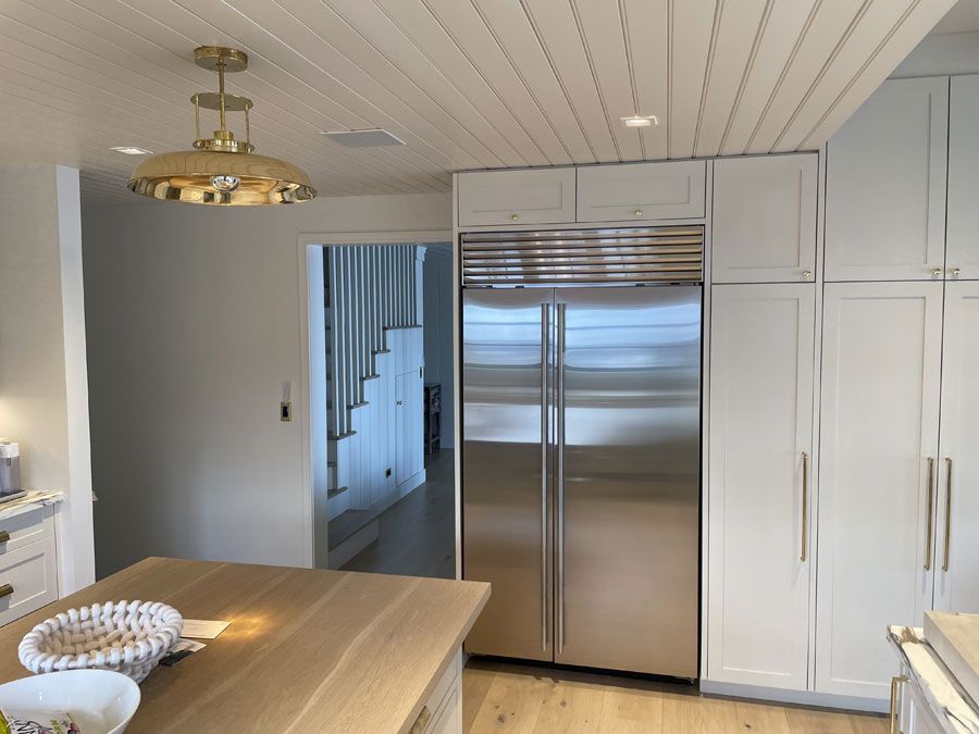 Modern kitchen with stainless steel fridge, white cabinets, and a wooden island under brass pendant lights