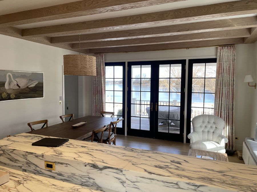 Bright dining room with marble island, wood beams, black-framed doors, and view of water outside