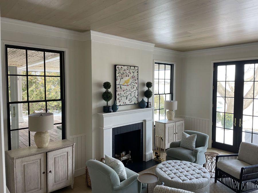 Bright living room with white fireplace, tall windows, and light blue chairs and ottoman