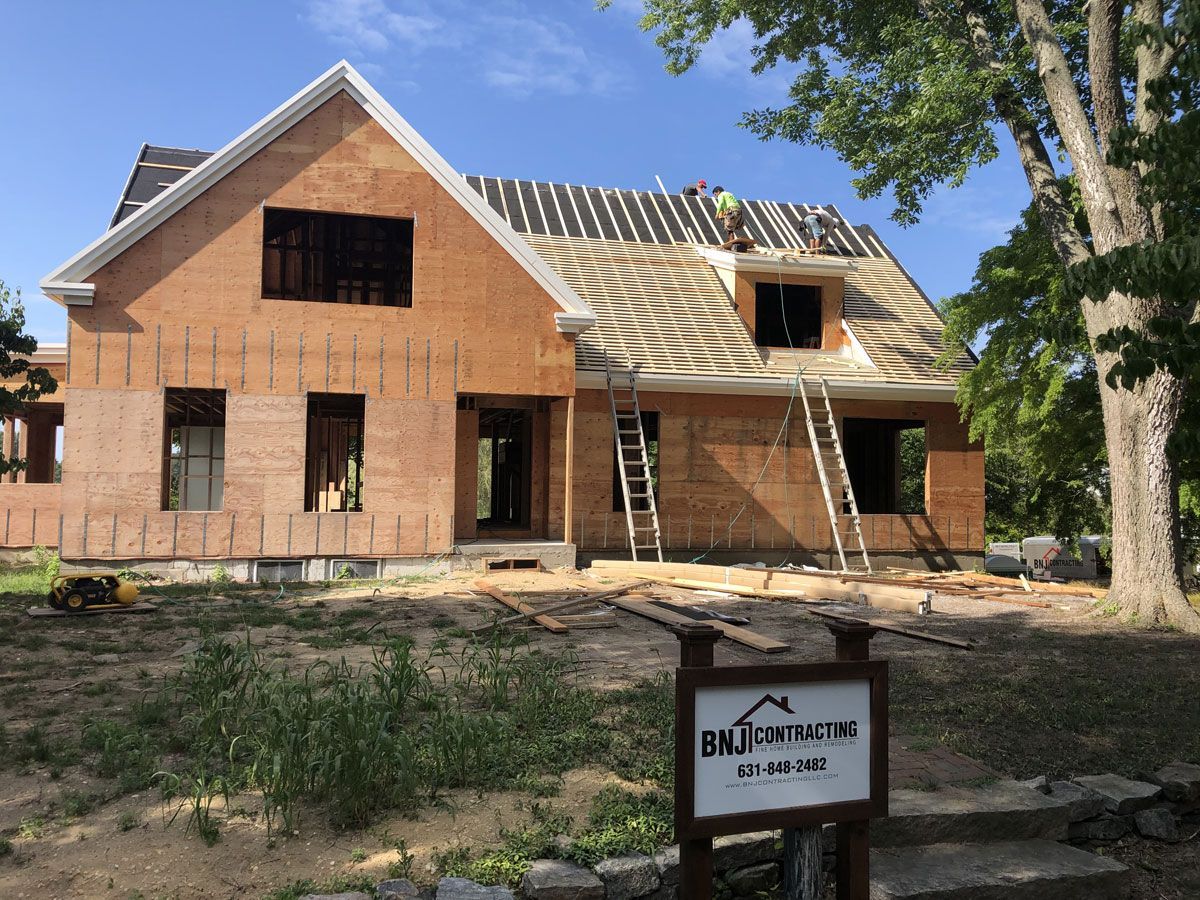 Partially built brick house under construction with ladders and a yard sign in front