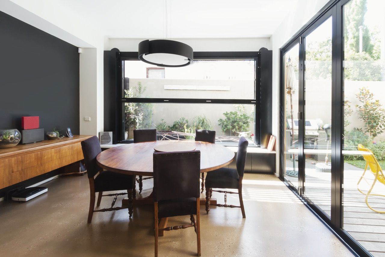 Salle à manger moderne avec table en bois, chaises noires, grandes fenêtres et lumière naturelle abondante