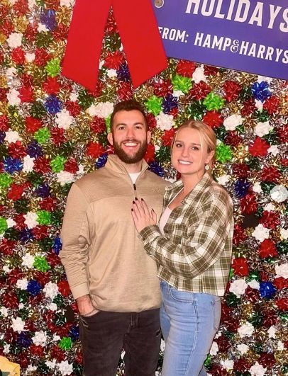 Couple posing in front of a holiday backdrop. The woman has her hand on the man's arm.