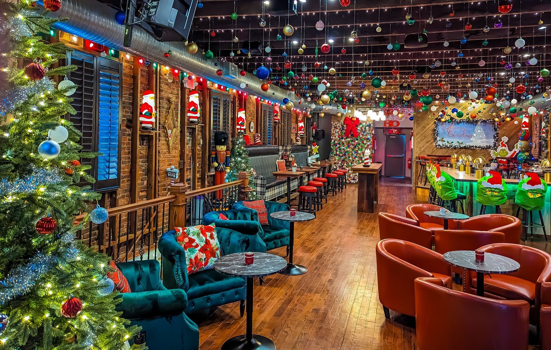 Festively decorated bar for the holidays. Christmas trees, lights, and ornaments. Seating areas with red and teal furniture.