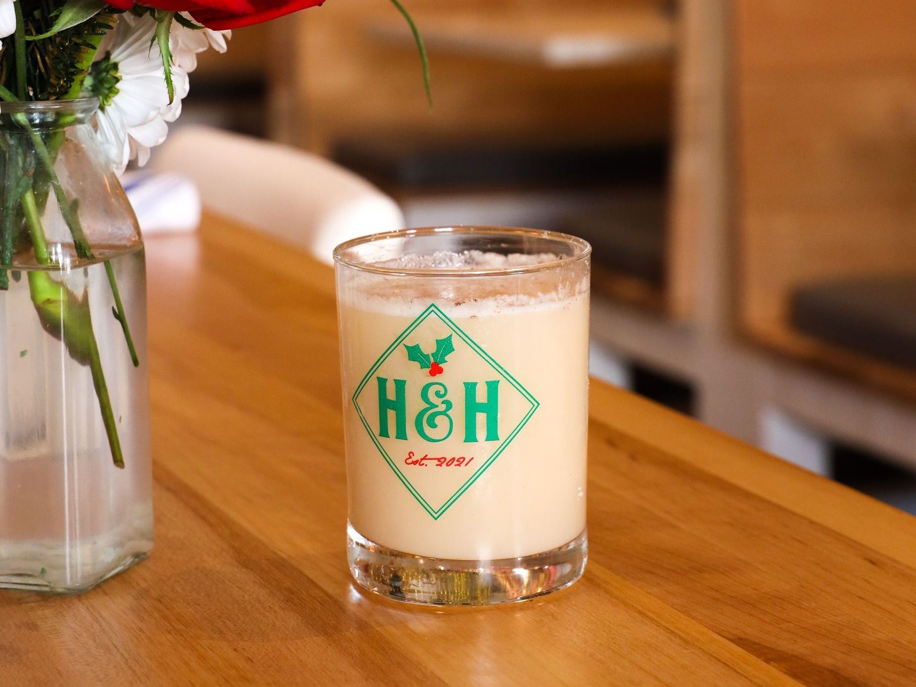 a glass of H & H eggnog sits on a wooden table a glass of H & H eggnog sits on a wooden table