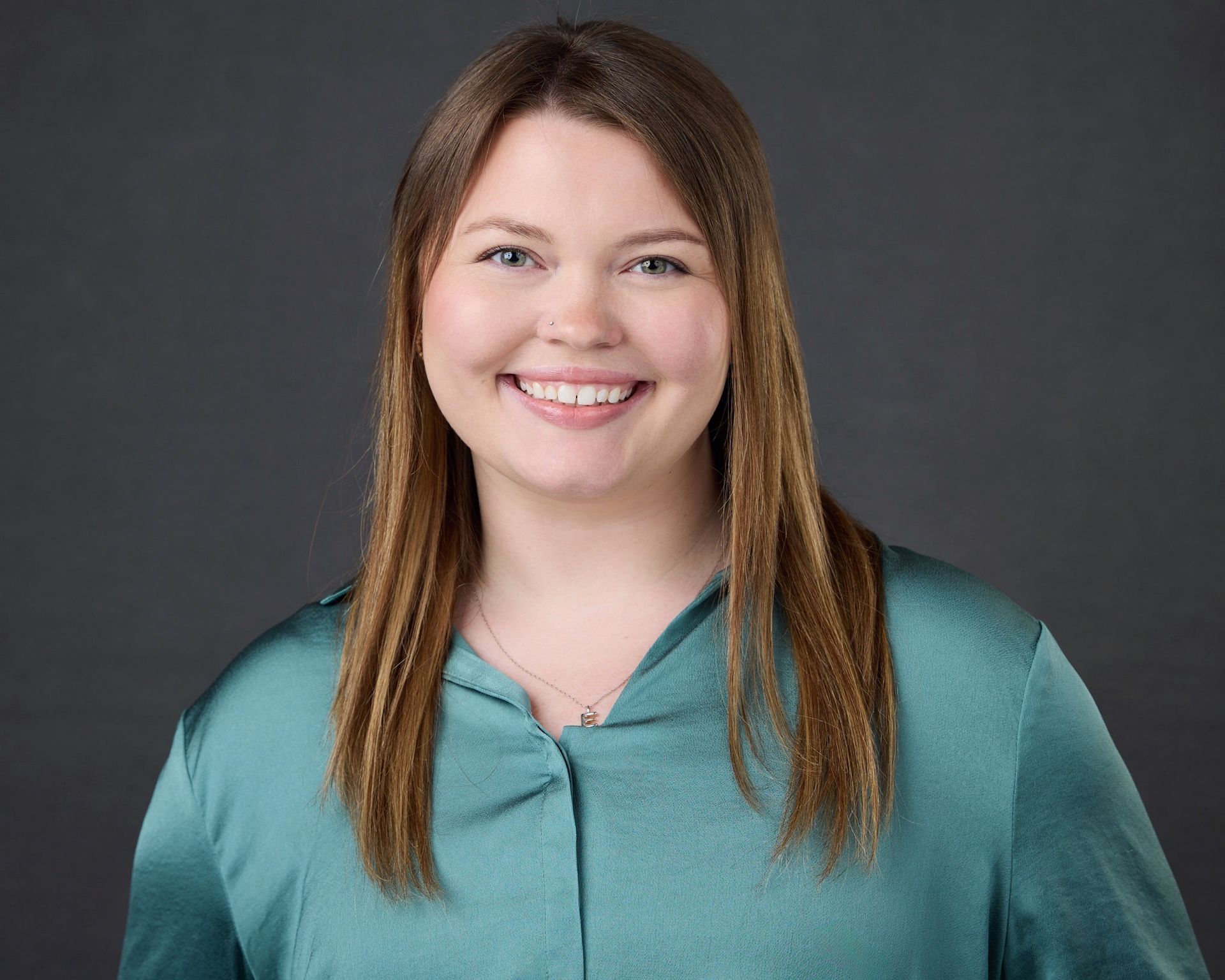 Smiling woman in teal blouse against a gray studio background