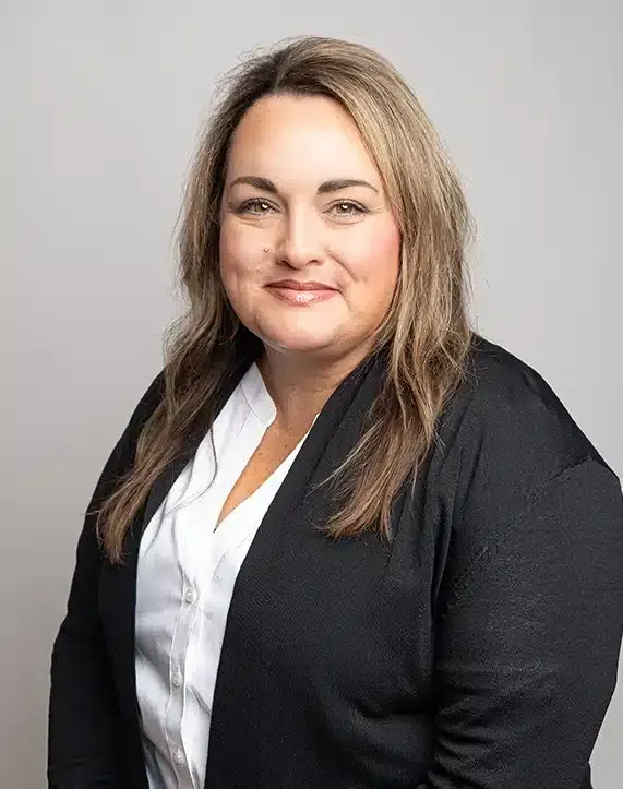 Professional headshot of a person in a black blazer and white blouse against a gray background