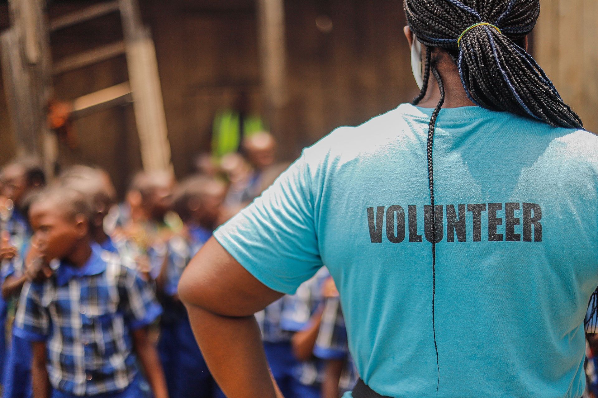 Volunteer in a blue shirt standing before a blurred crowd at an outdoor event