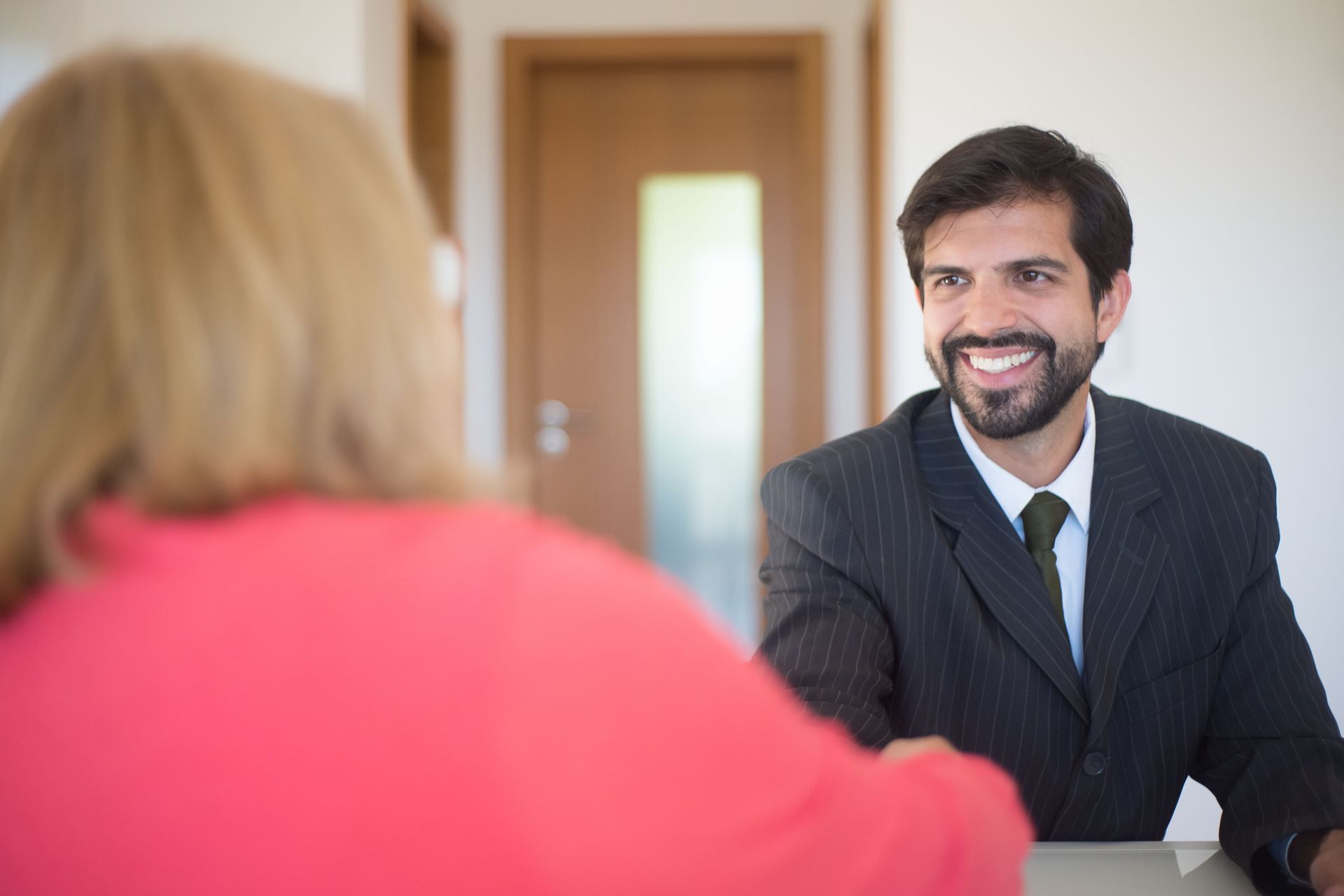 Smiling man in a suit talking with a woman across a desk in an office