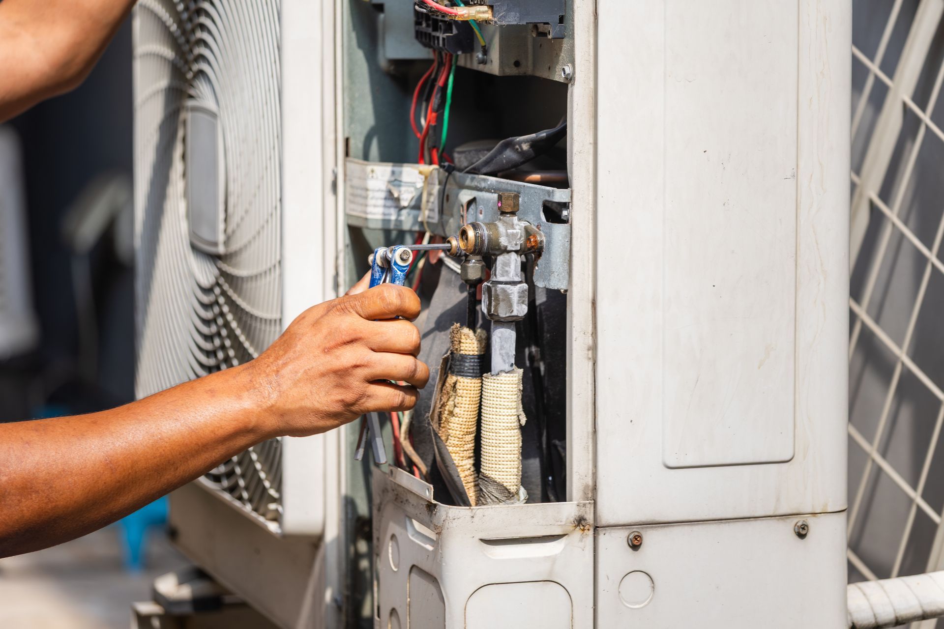 Technician using a screwdriver to service an outdoor AC condenser unit's internal wiring Technician using a screwdriver to service an outdoor AC condenser unit's internal wiring