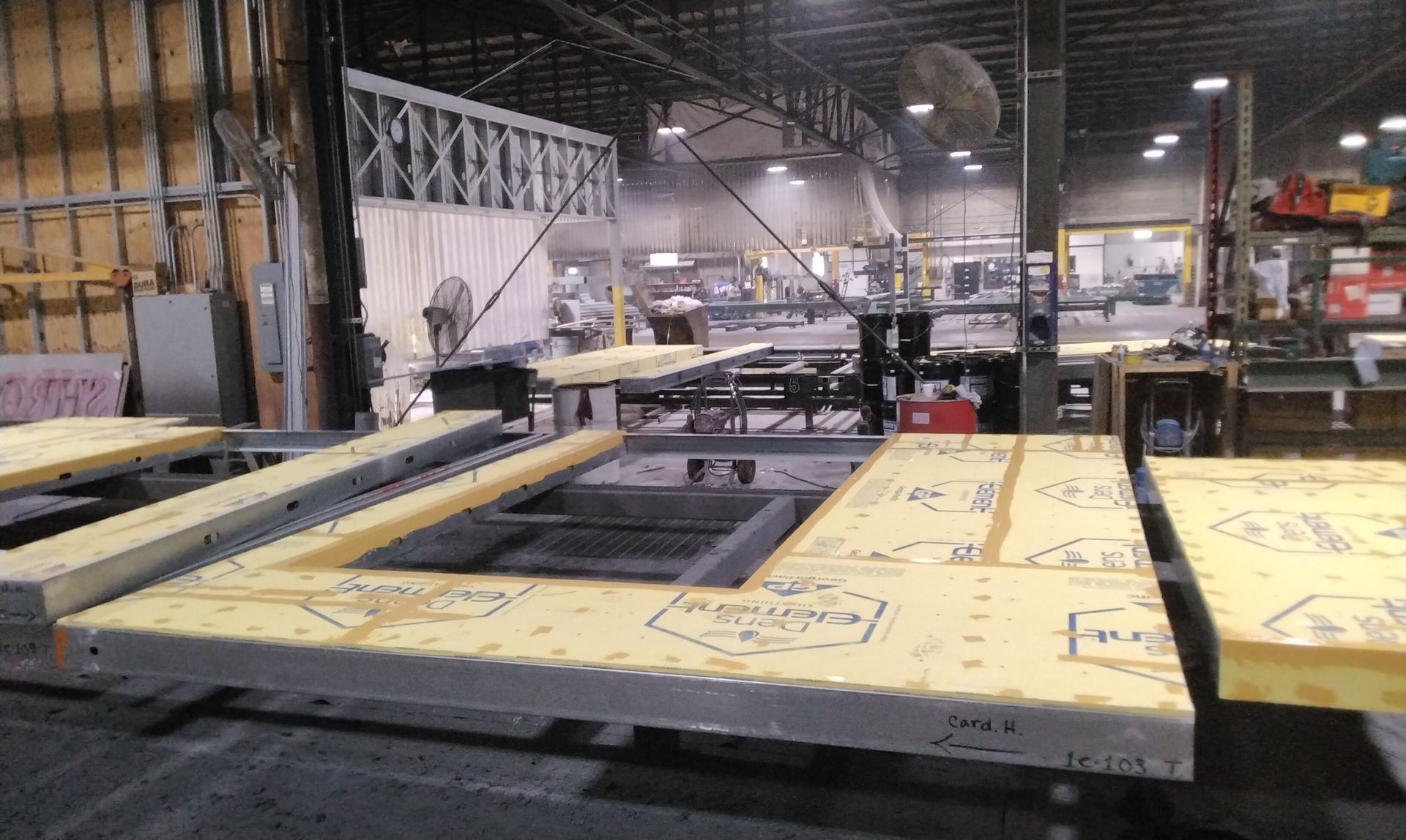 Industrial factory floor with large yellow sheet material on machinery and workers in the background.