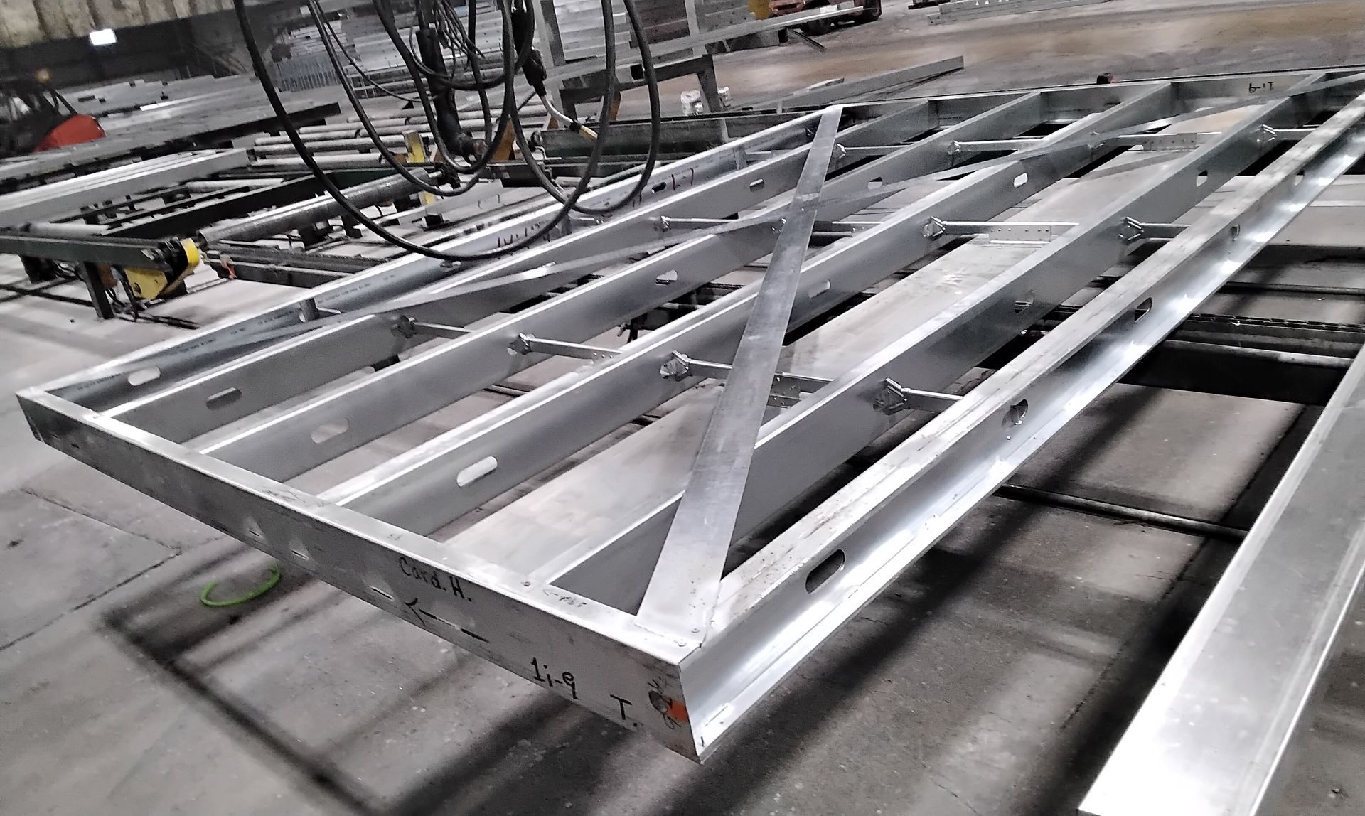 Silver metal framework on a factory conveyor line with cables overhead.