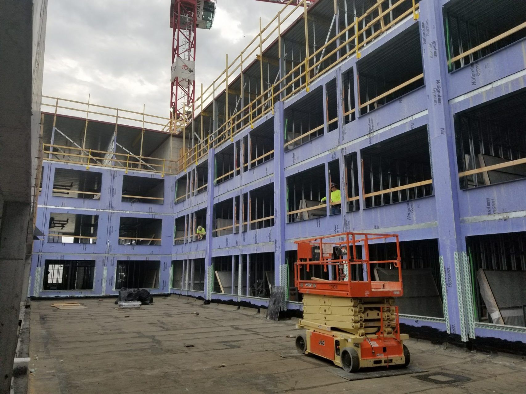 An orange scissor lift is parked in front of a building under construction.