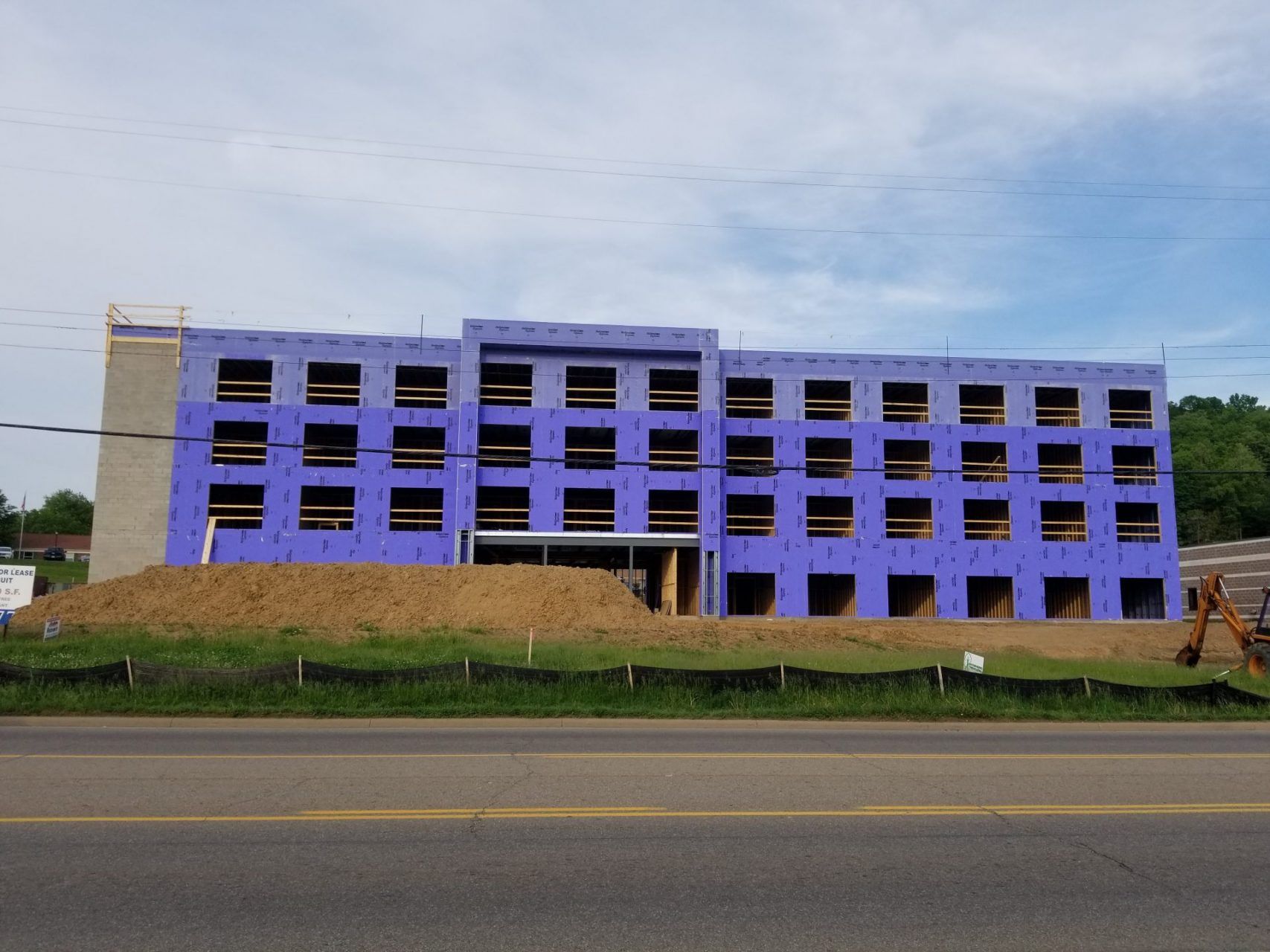 A large building is under construction on the side of the road with purple insulation panels.