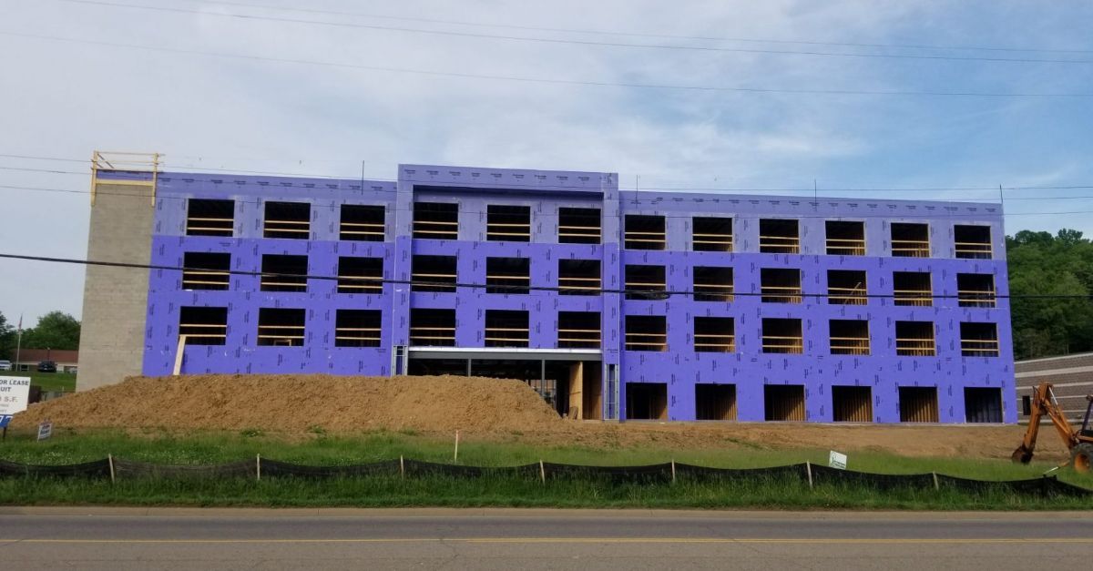 A large building with purple insulation panels is being built next to a road.