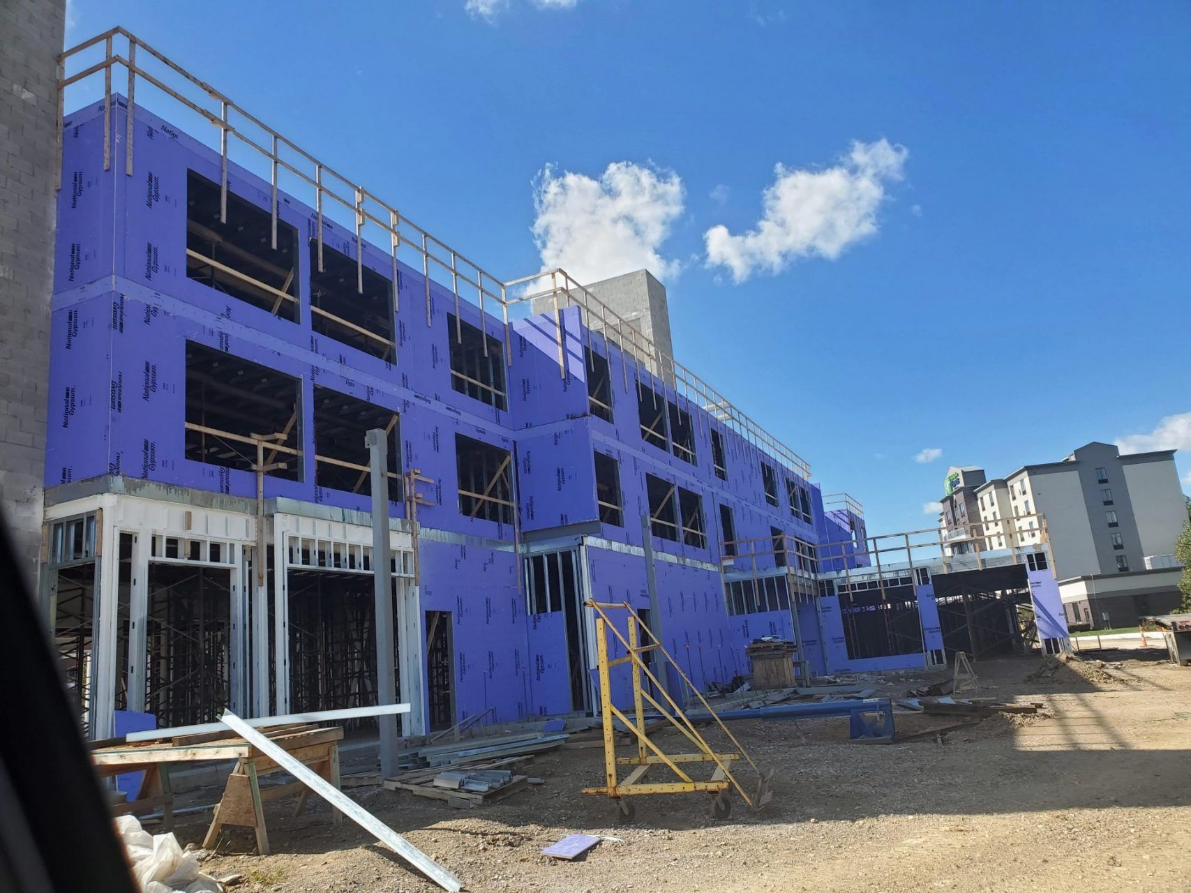 A large building is being built with large steel panels being construction with purple insulation panels.