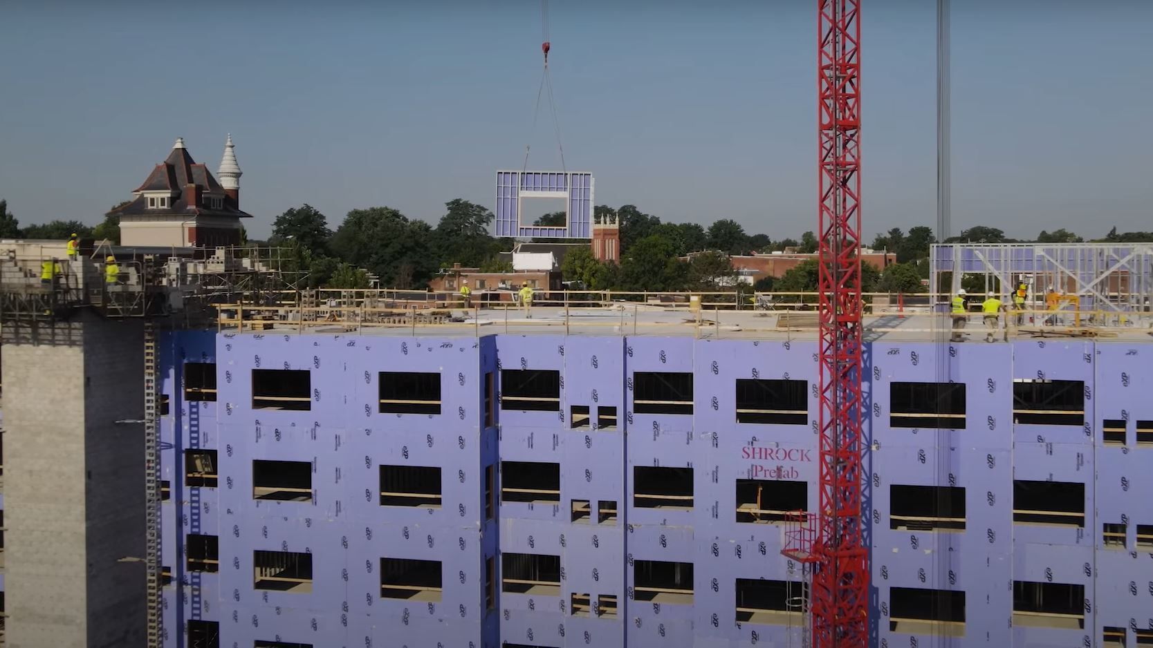 An aerial view of a building under construction with a red crane in the foreground.