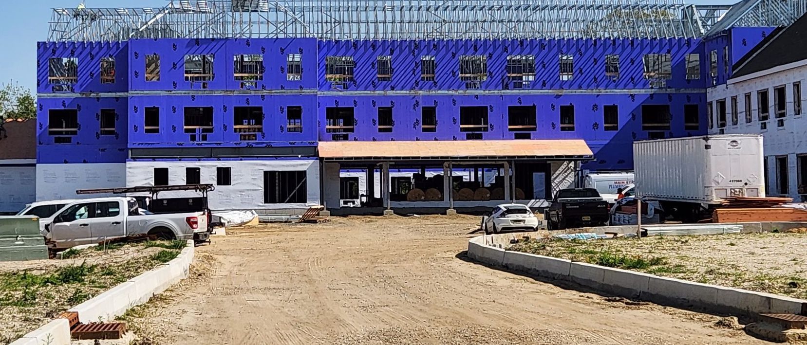 A large blue building under construction with vehicles parked in front of it.