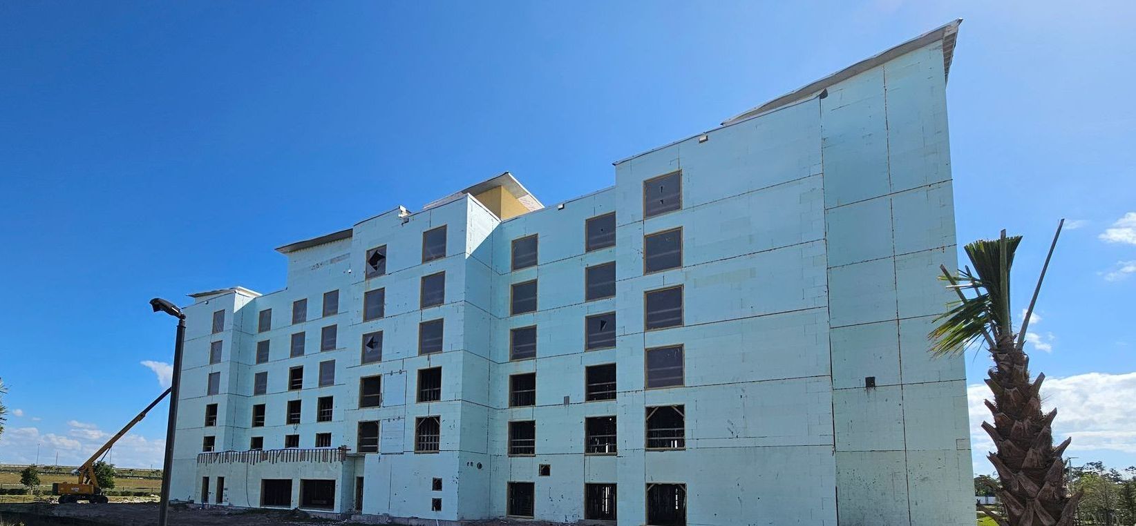 A large white building under construction with a palm tree in front of it.