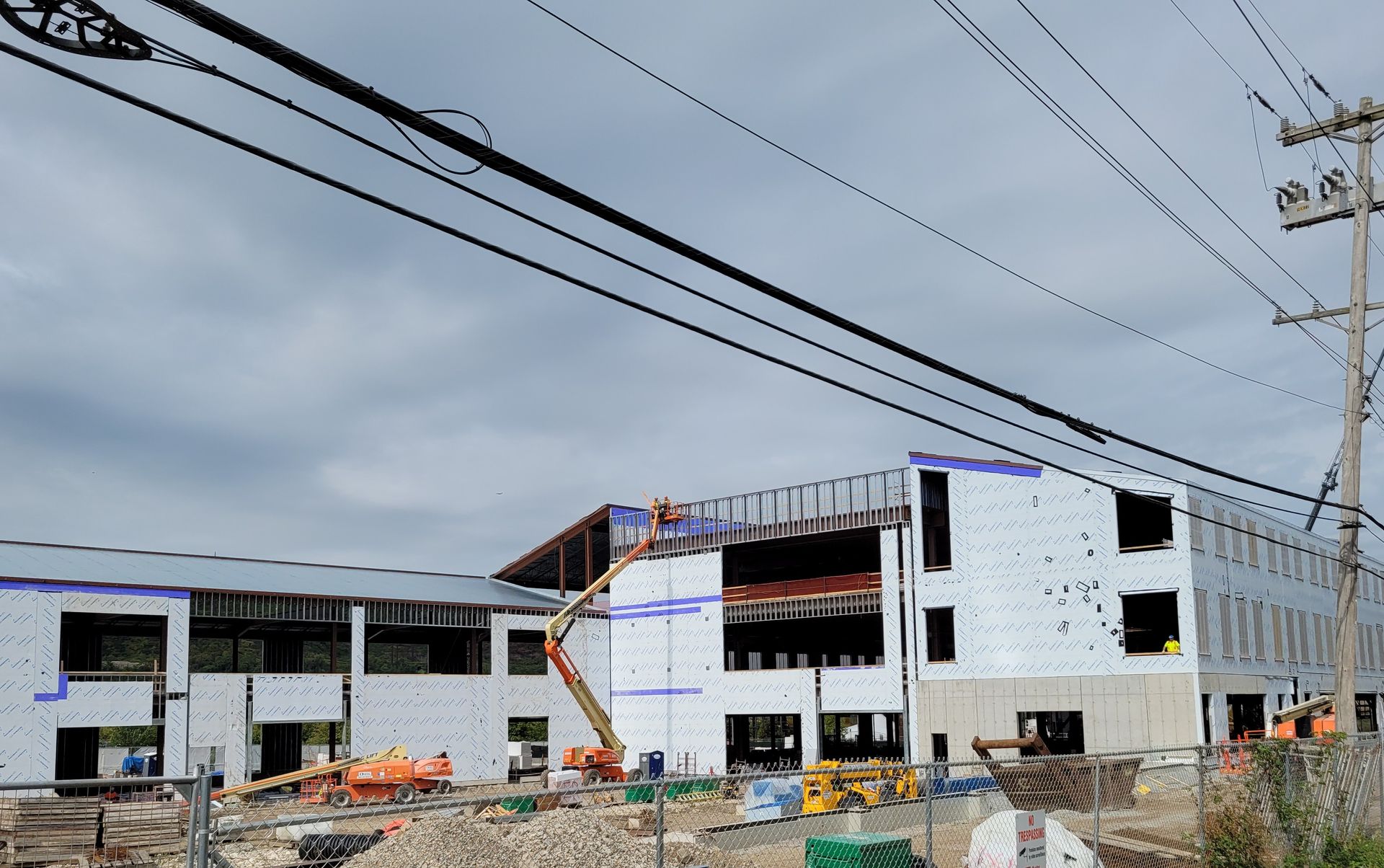 Construction site with unfinished white buildings, scaffolding, and power lines under a cloudy sky