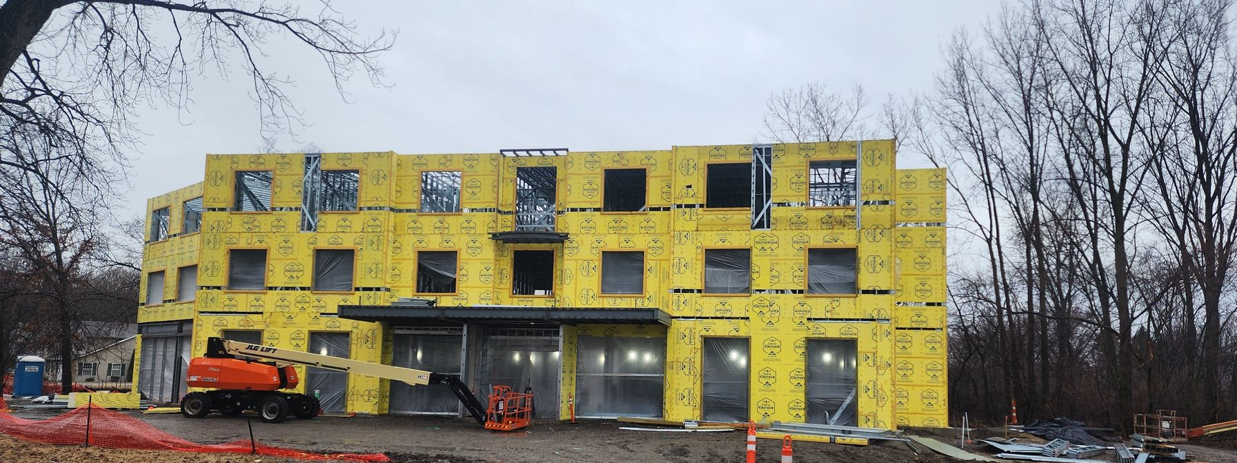 Yellow building under construction with scaffolding, windows, and construction vehicles in front.