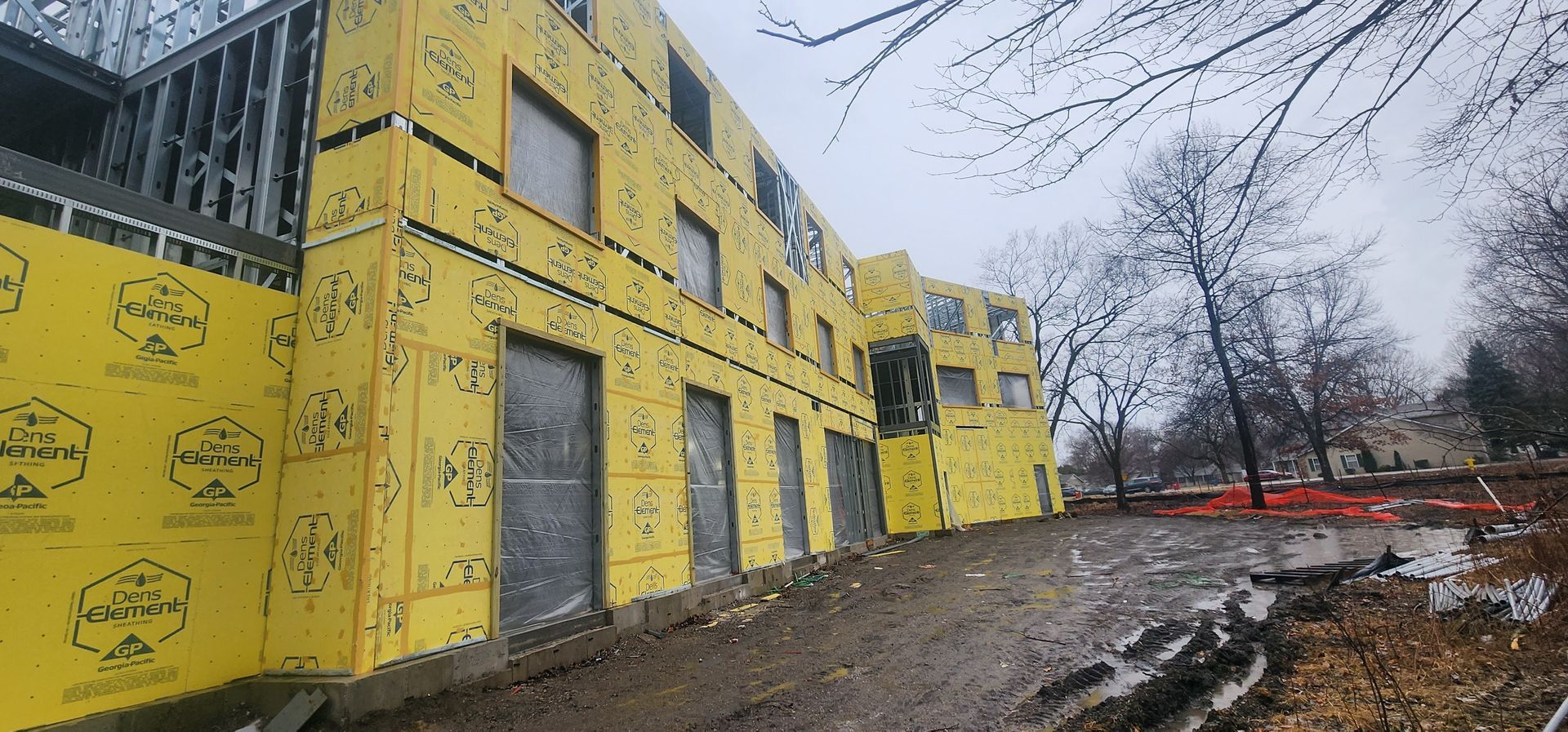 Yellow building under construction beside a muddy path on an overcast day.