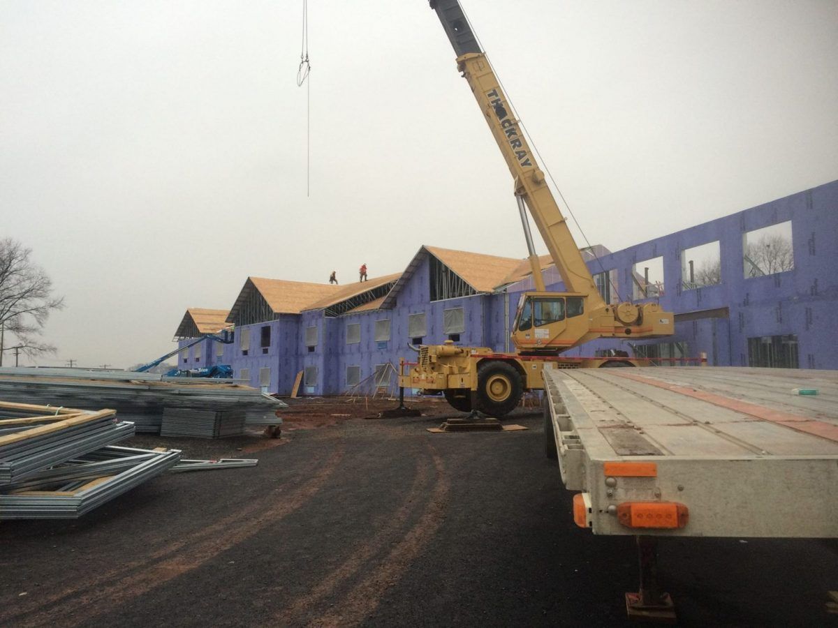 A large yellow crane is being used in front of a building under construction.