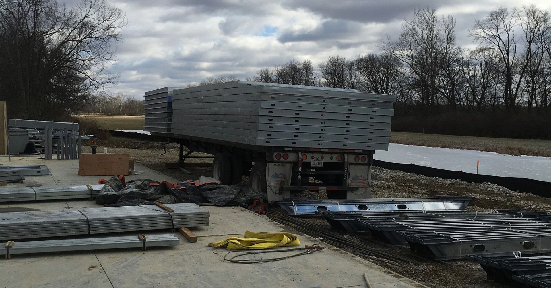 A large stack of lumber is sitting on top of a trailer. There are bundles of steel in the picture as well.