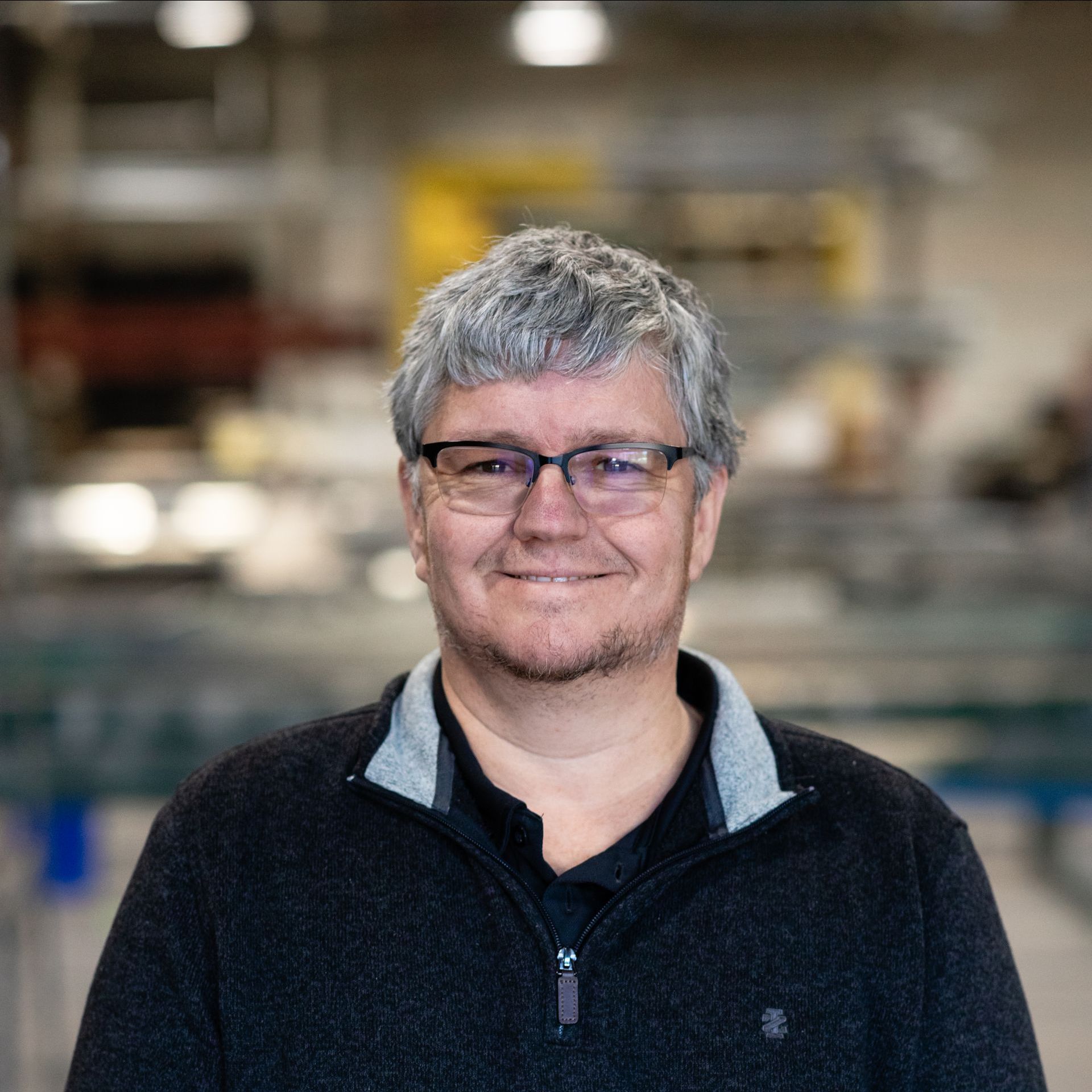 A man wearing glasses and a black sweater is smiling.