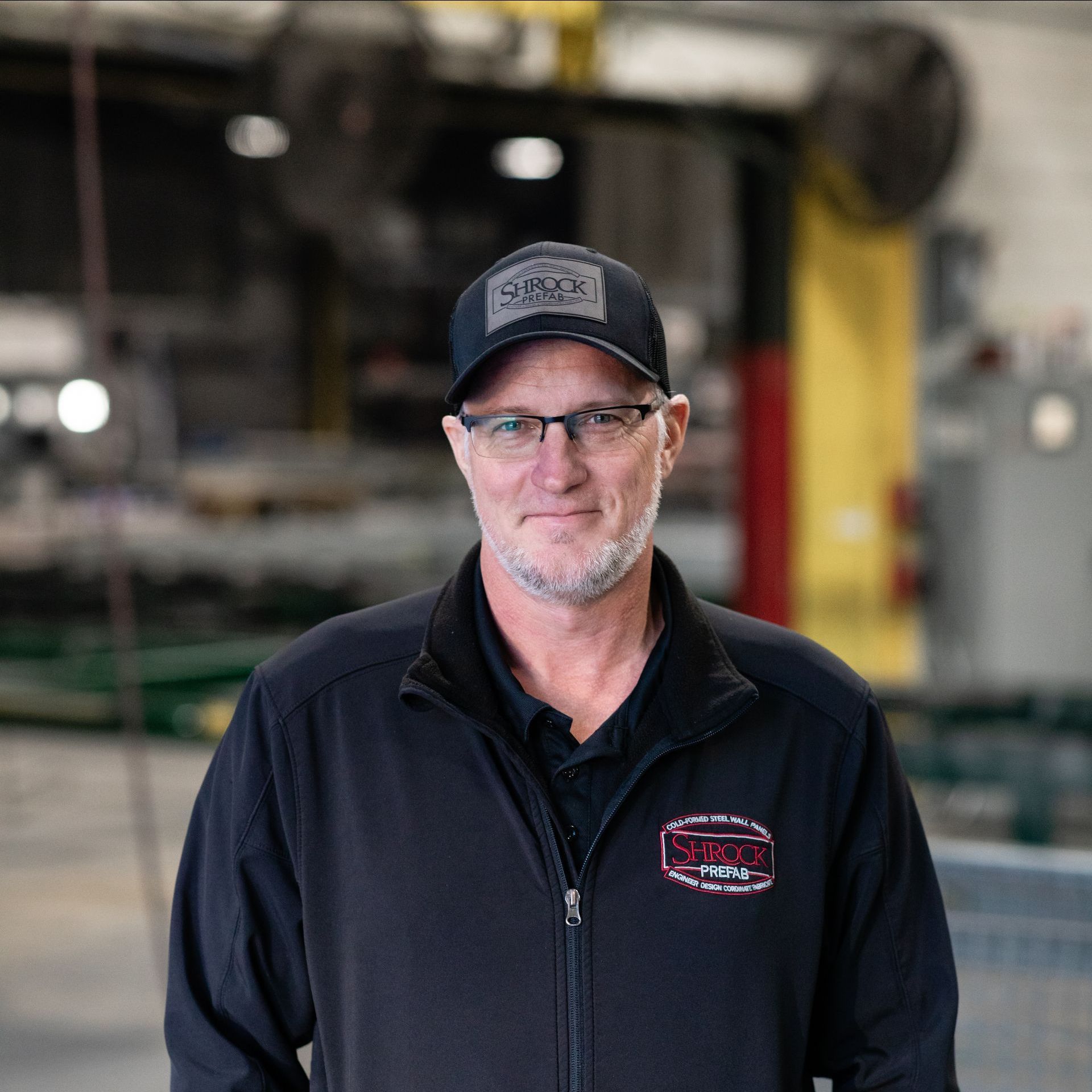 A man wearing a hat and glasses is standing in a garage.