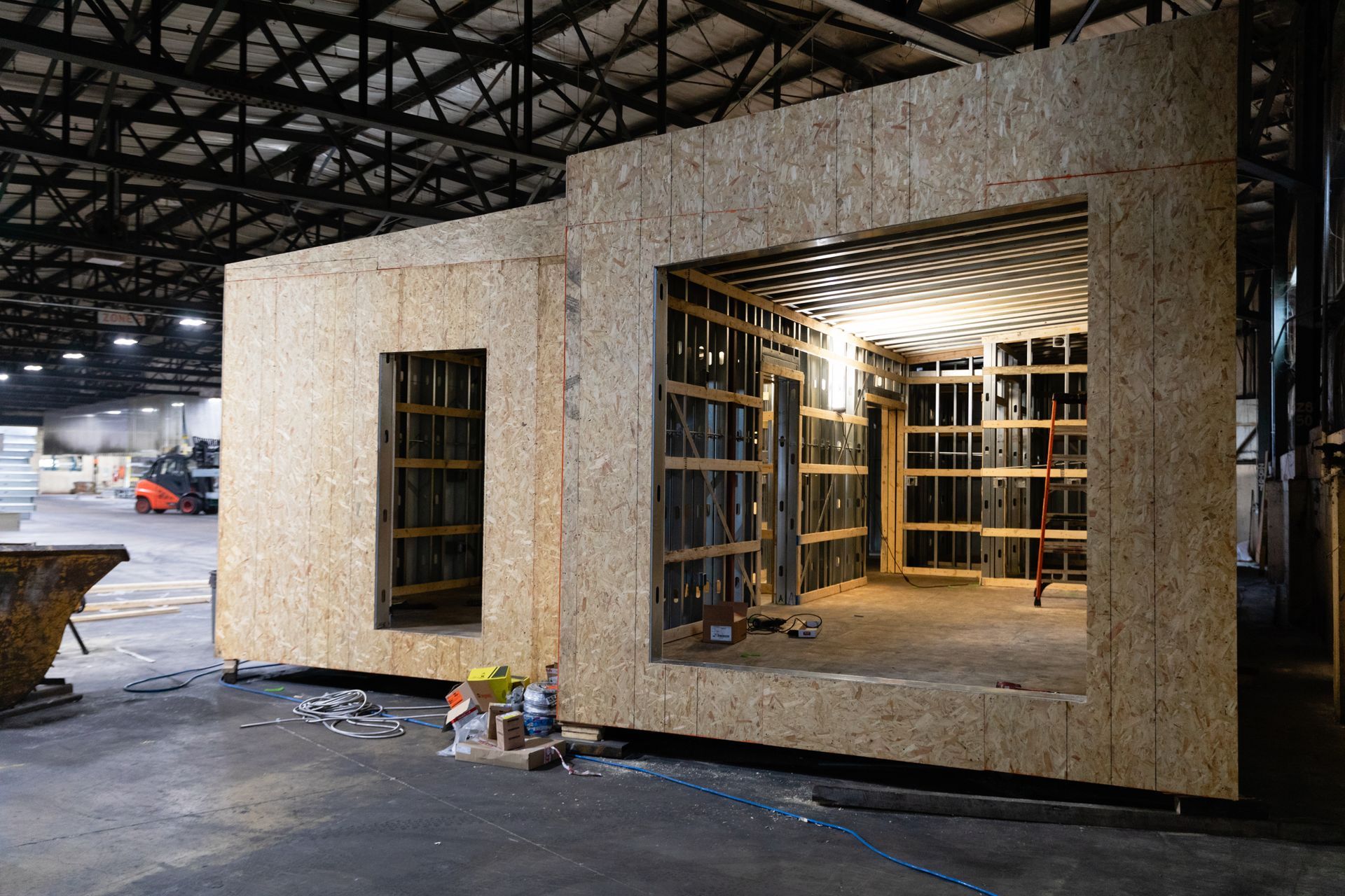 Small modular building under construction inside a warehouse, with open windows and exposed framing.