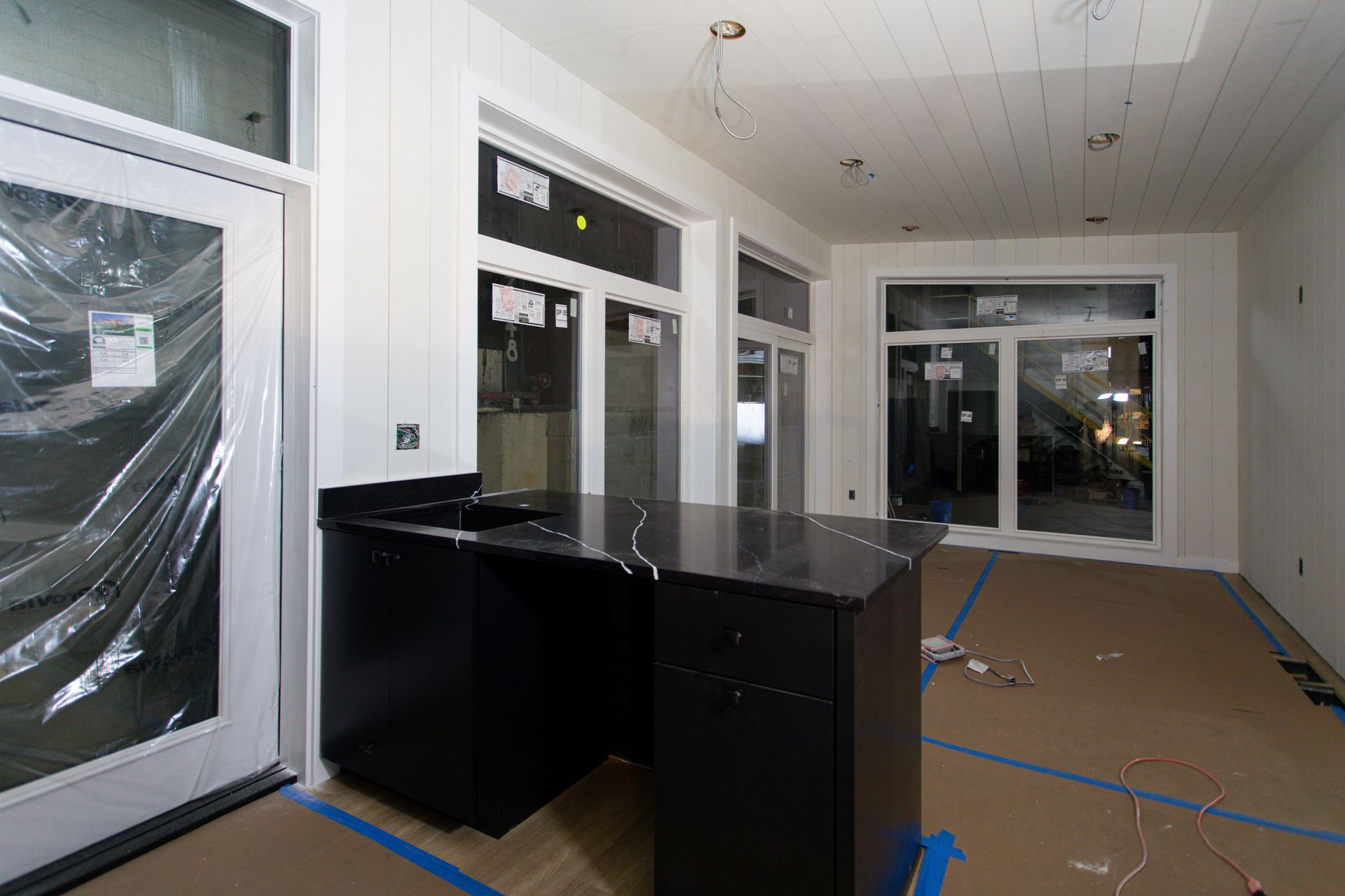 Empty room with white walls, black cabinets, and windows; floor covered with protective brown paper and blue tape.