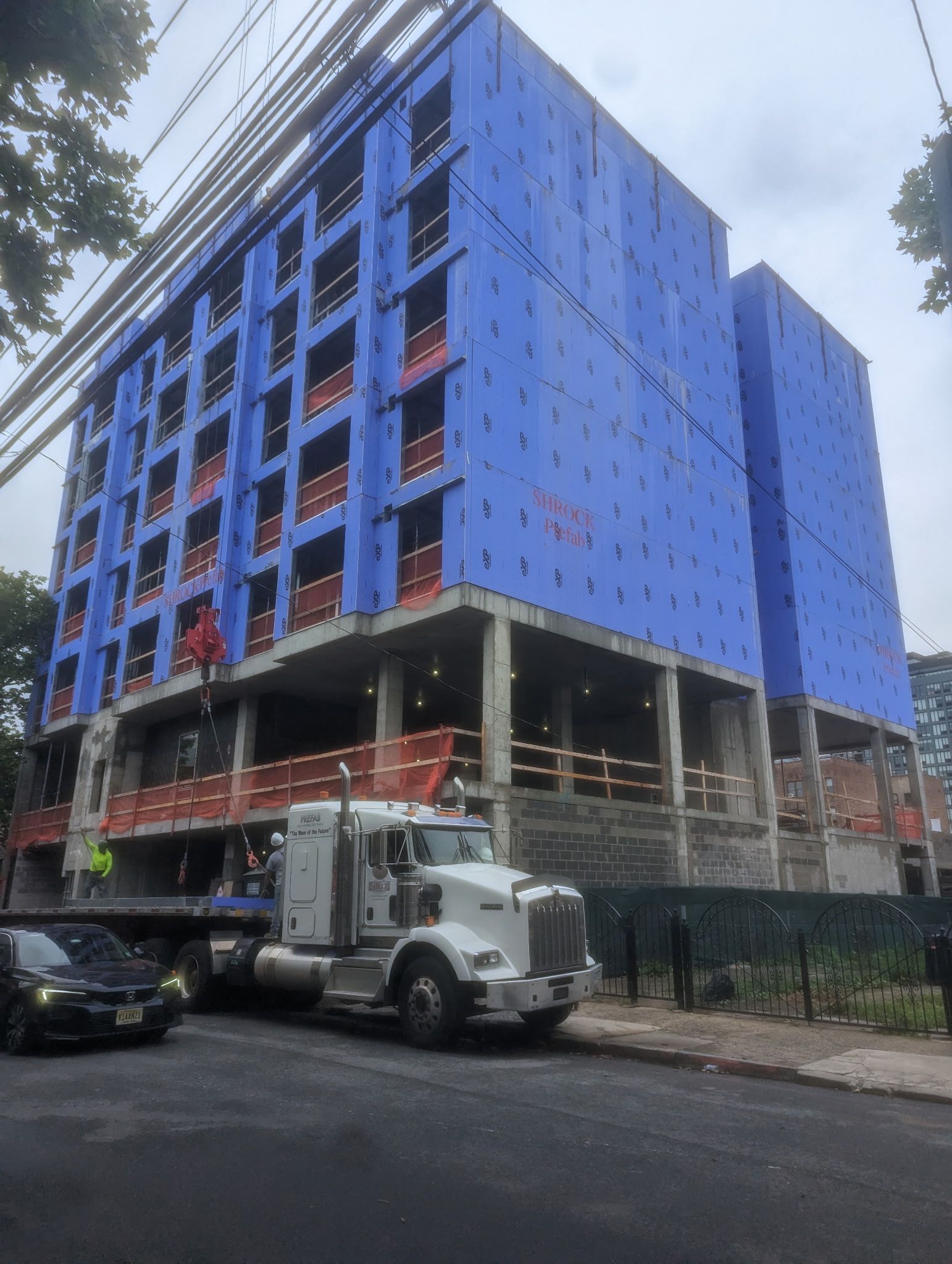 Blue-clad multi-story building under construction with a truck parked on the street below.