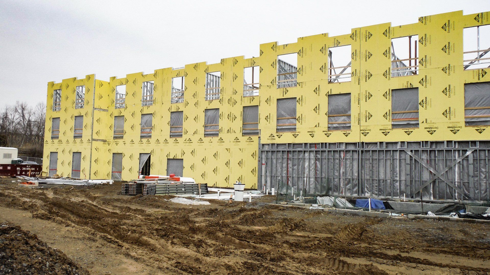 A large building under construction with a lot of window and yellow insulation panels. 