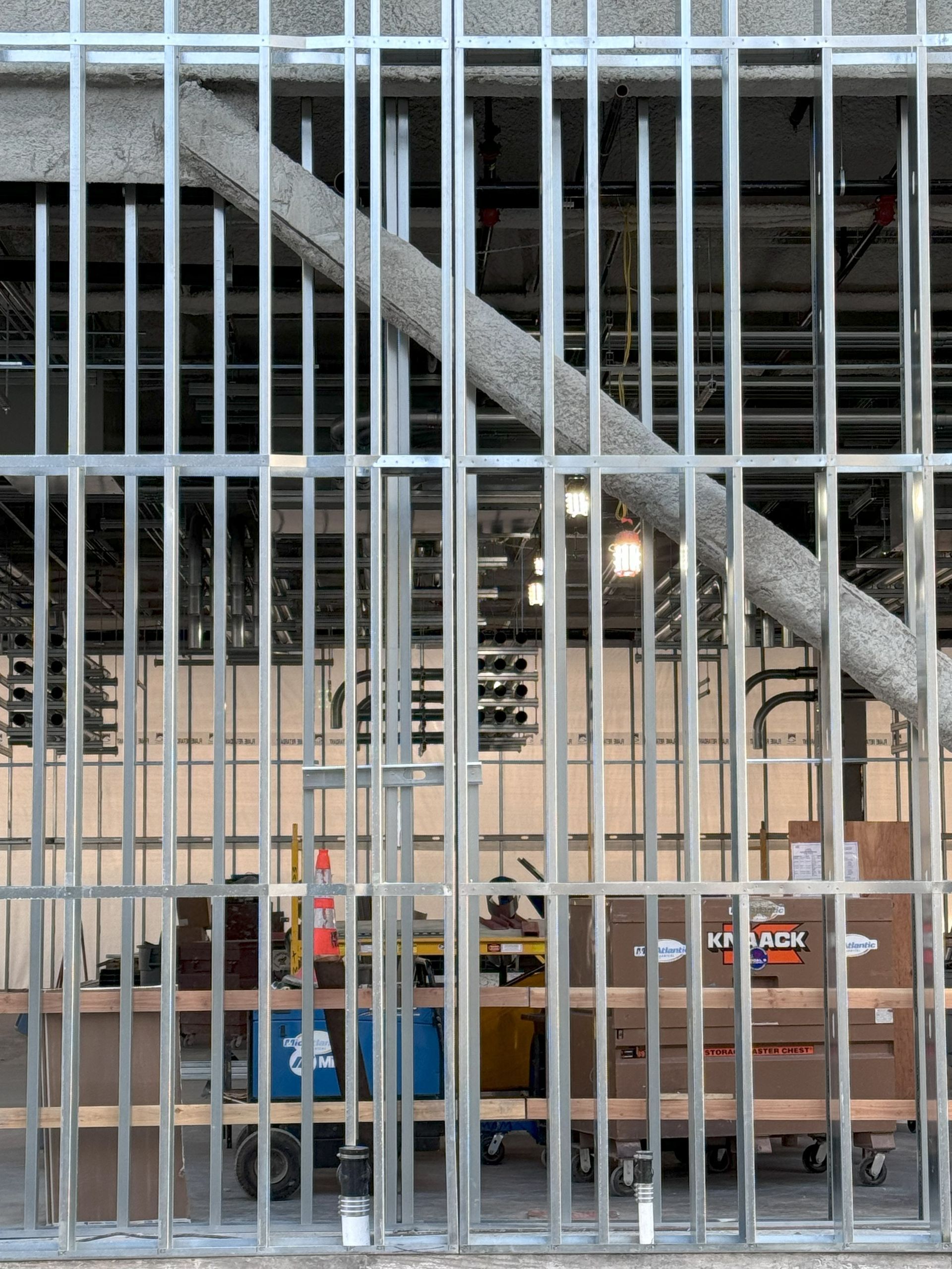 Metal security fence in front of a construction site with scaffolding and work tables inside.