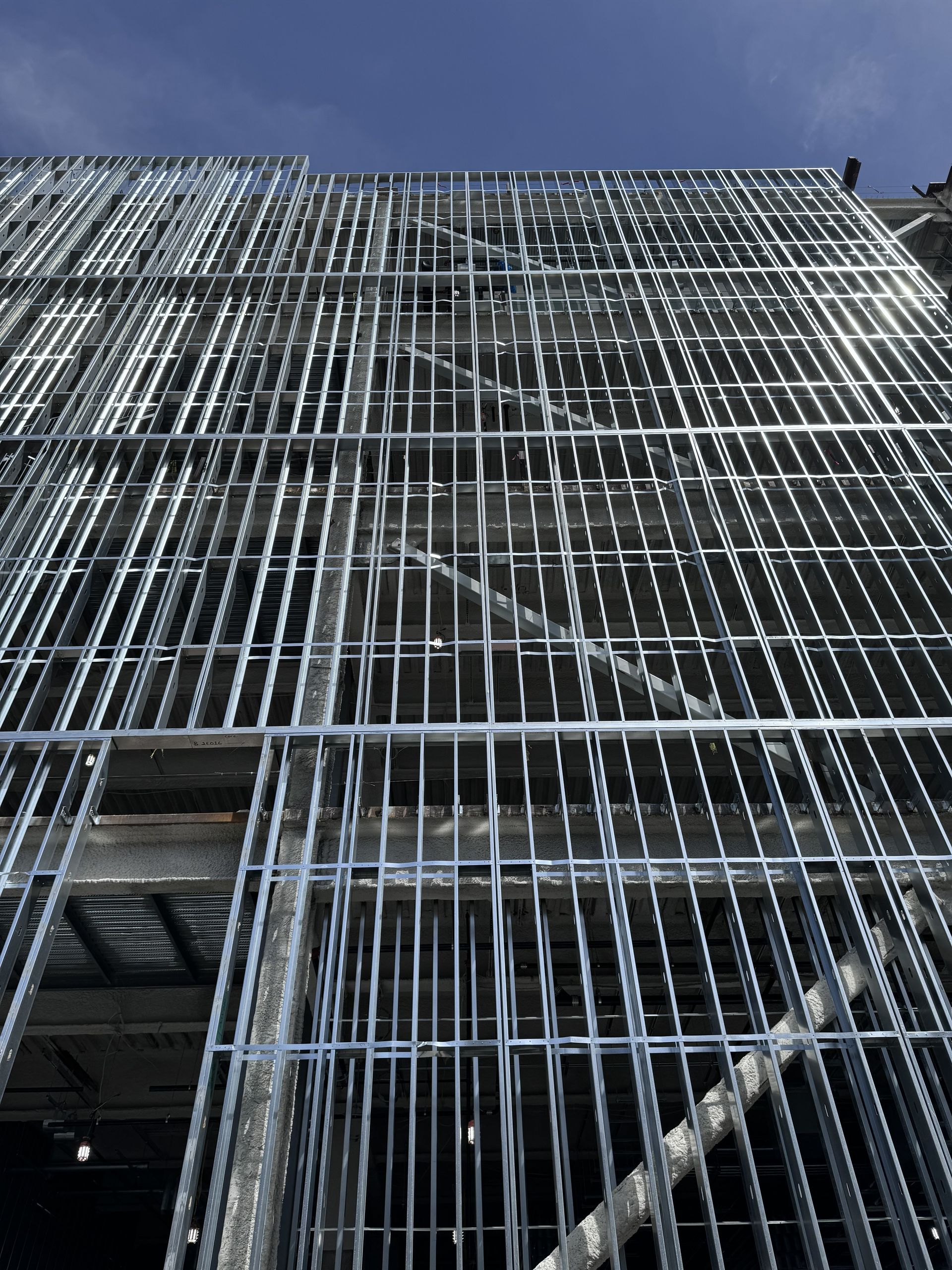 Metal scaffolding and safety netting cover the side of a tall building under a clear blue sky.