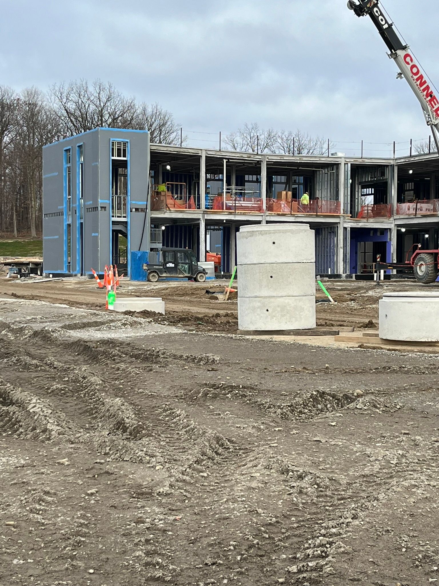 Construction site with a partially built multi-story building, blue exterior sheathing, and a crane arm visible.