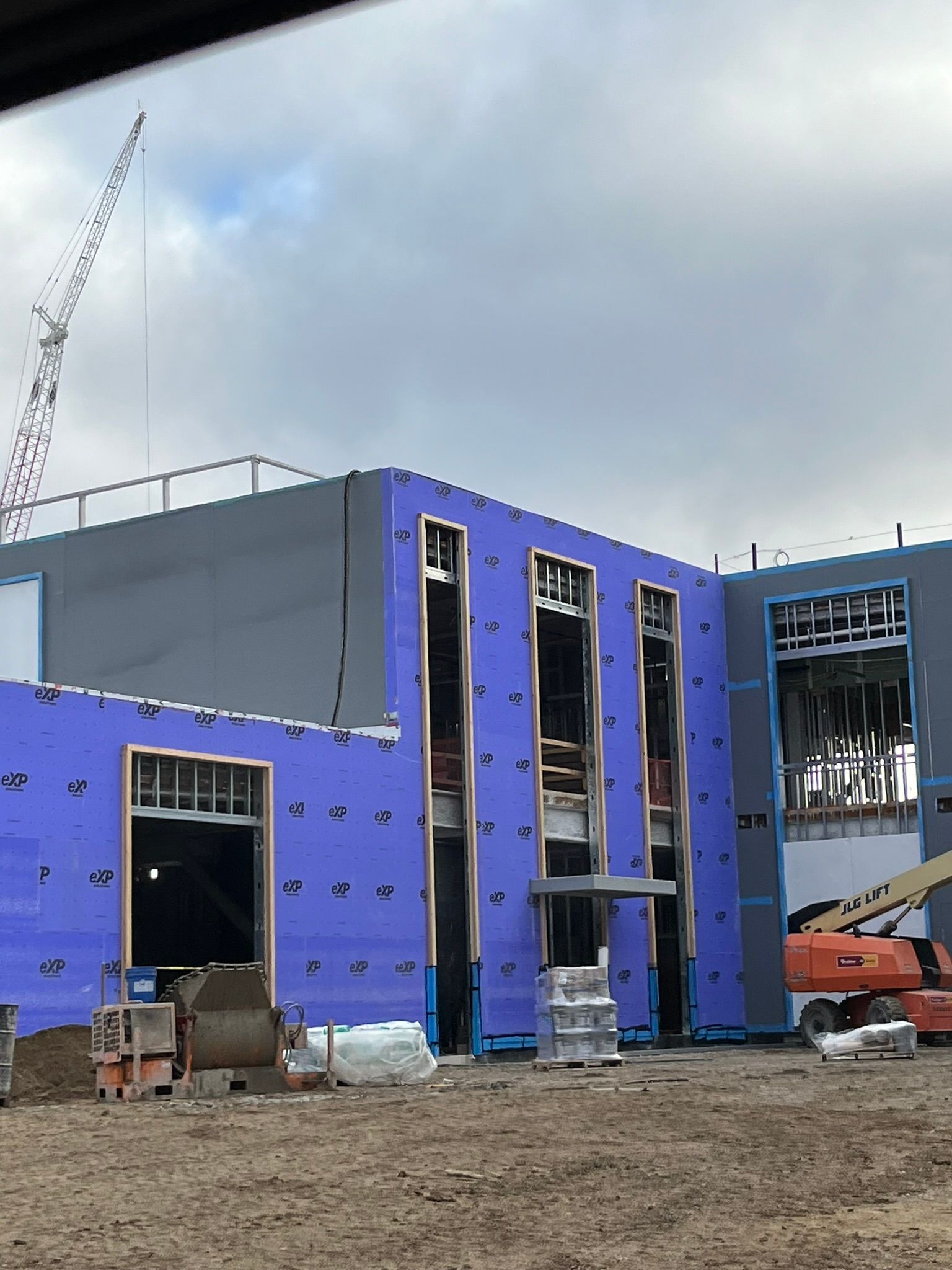 Multi-Level building under construction with exposed framing, tall window openings, and muddy ground.