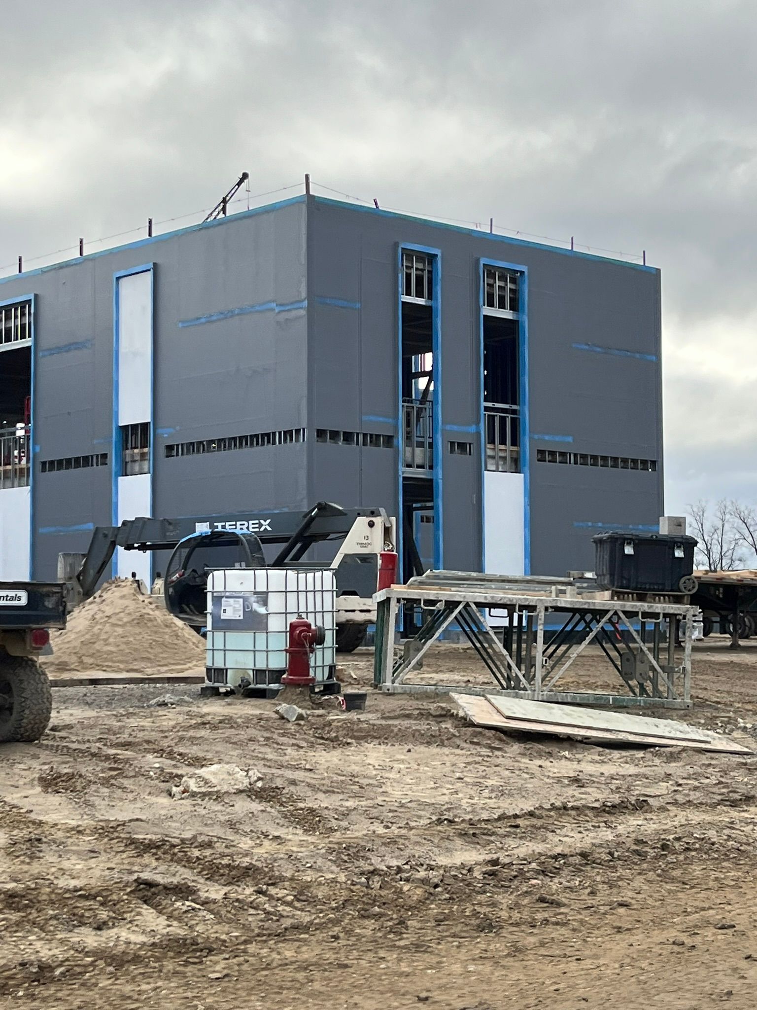 Gray industrial building under construction with dirt foreground and construction materials.