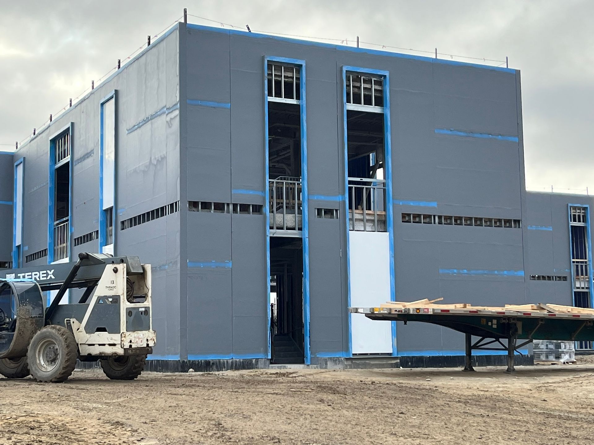 Industrial building under construction with blue-gray siding, a lift, and a work platform outside.