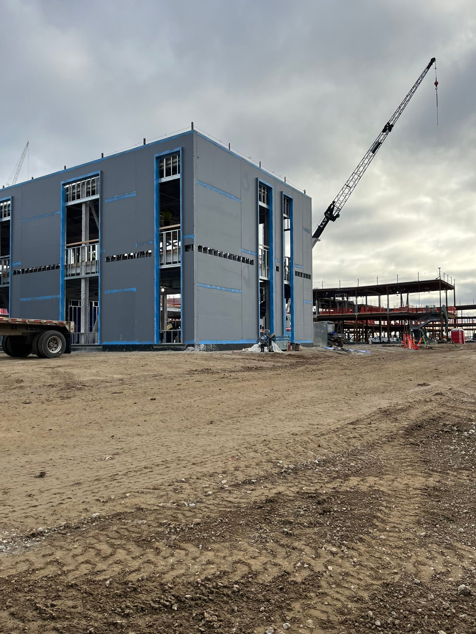 Blue modular building sections at a construction site with a crane under an overcast sky.