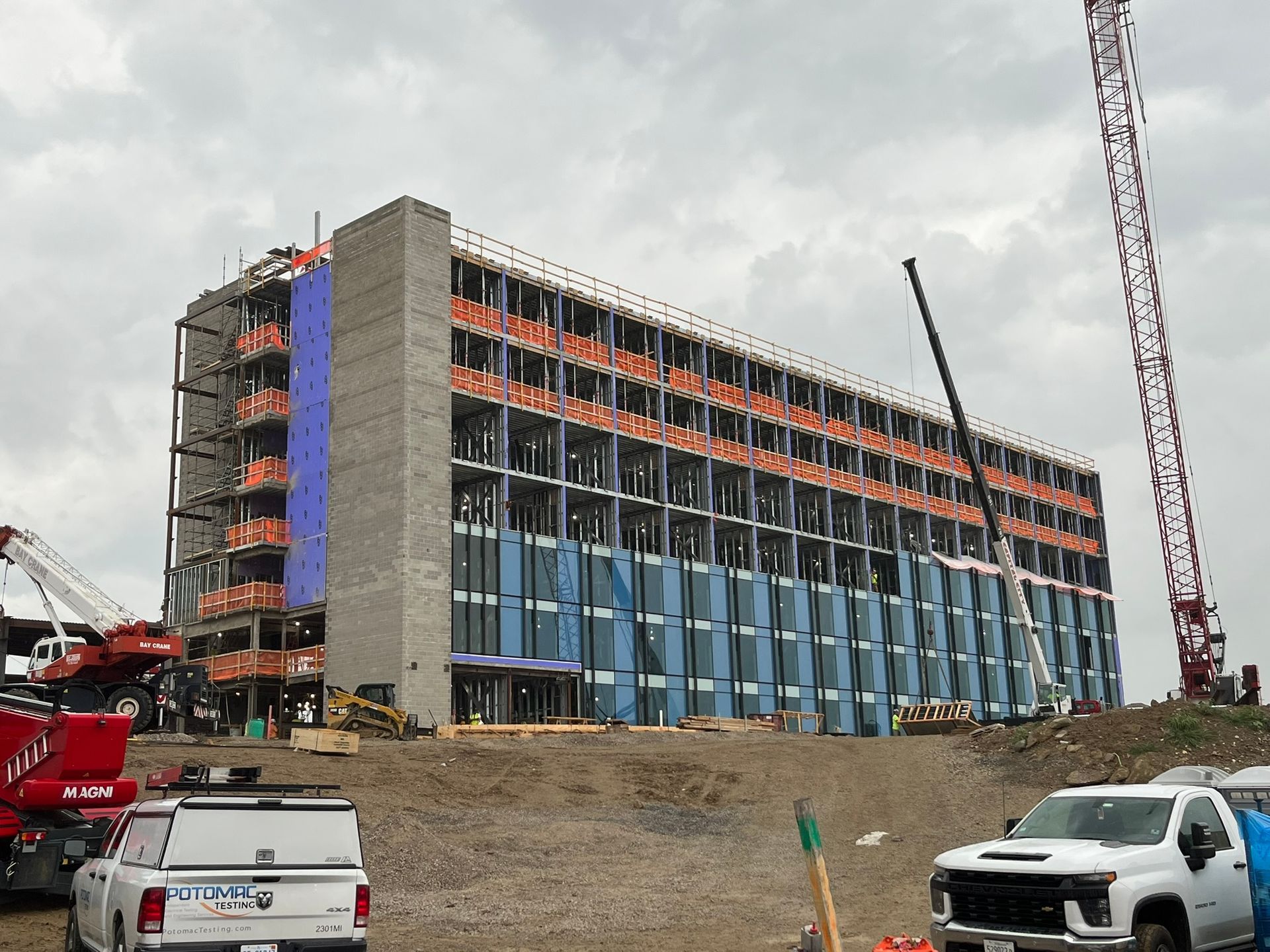 Partially built multi-story building at a construction site, with trucks and cranes nearby.