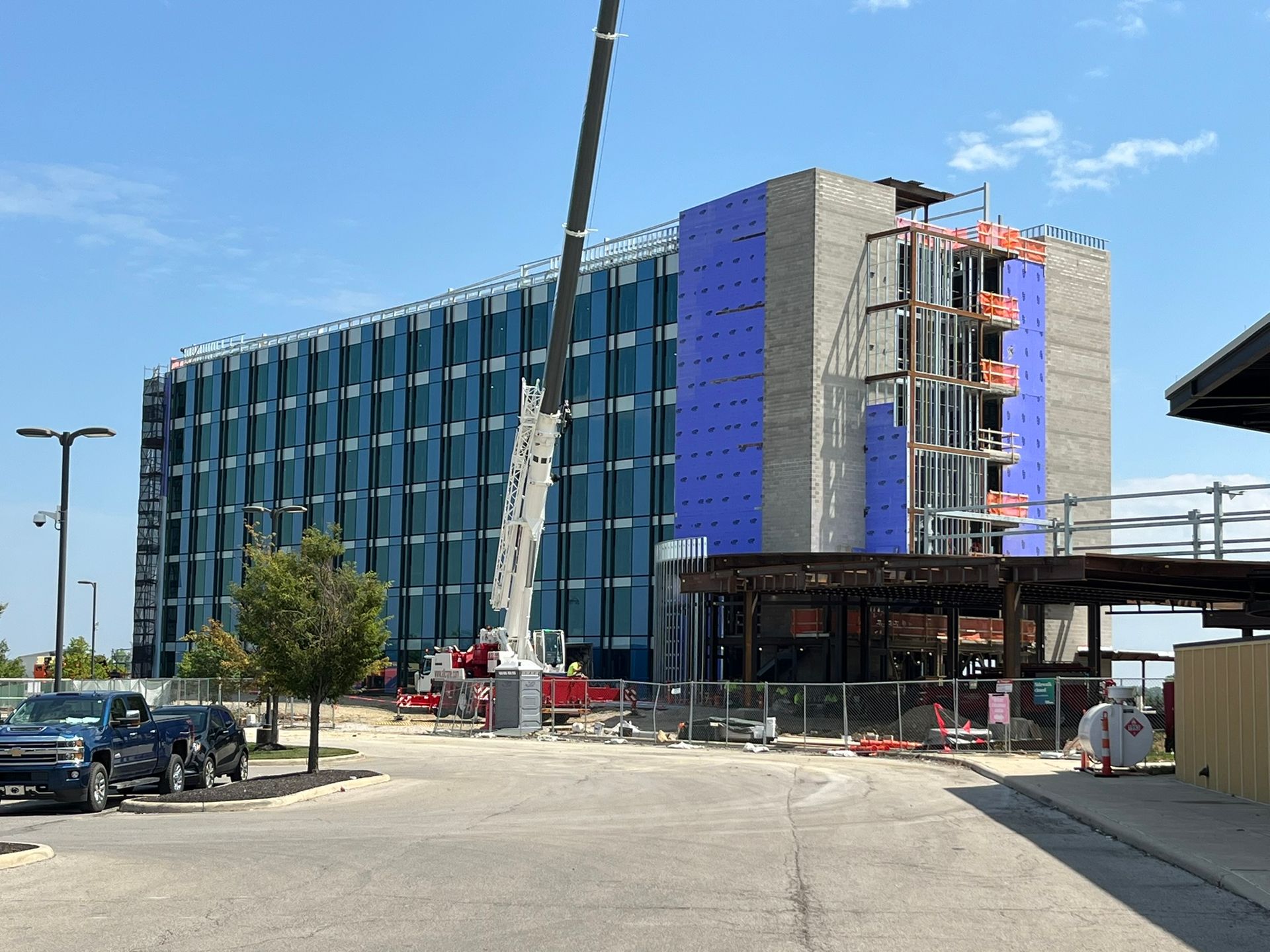 Construction site with a partly finished blue building, crane, and parked cars under a clear sky.