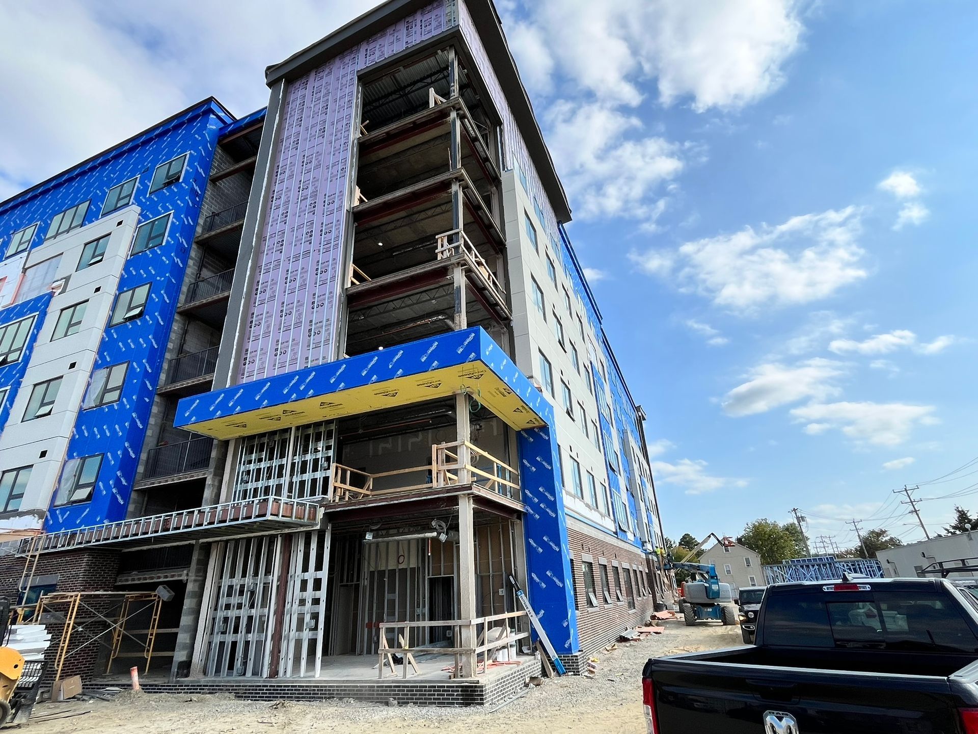 Partially built multi-story building with blue tarp and scaffolding under a bright sky.