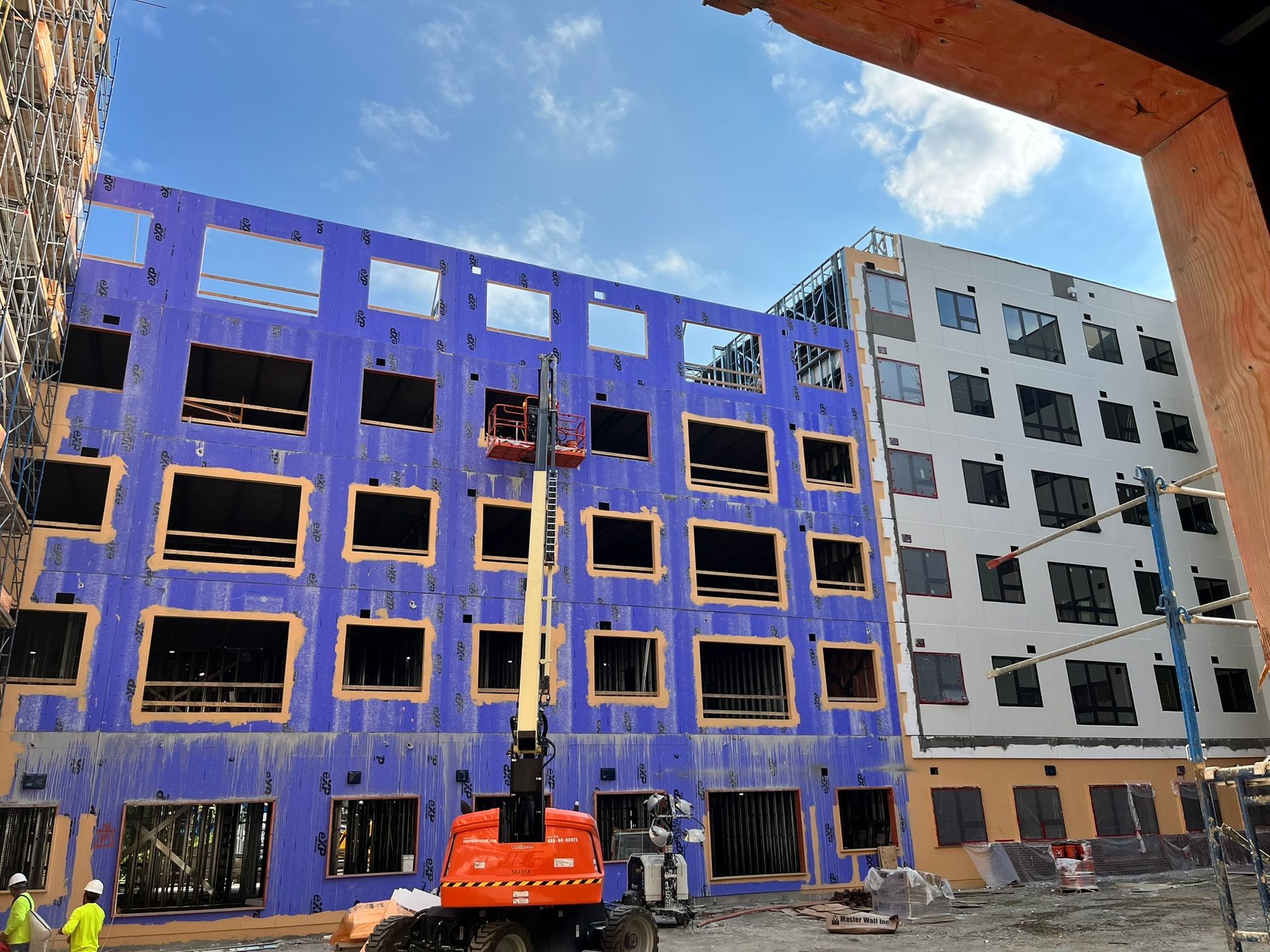 Blue and gray apartment buildings under construction with an orange lift in front.