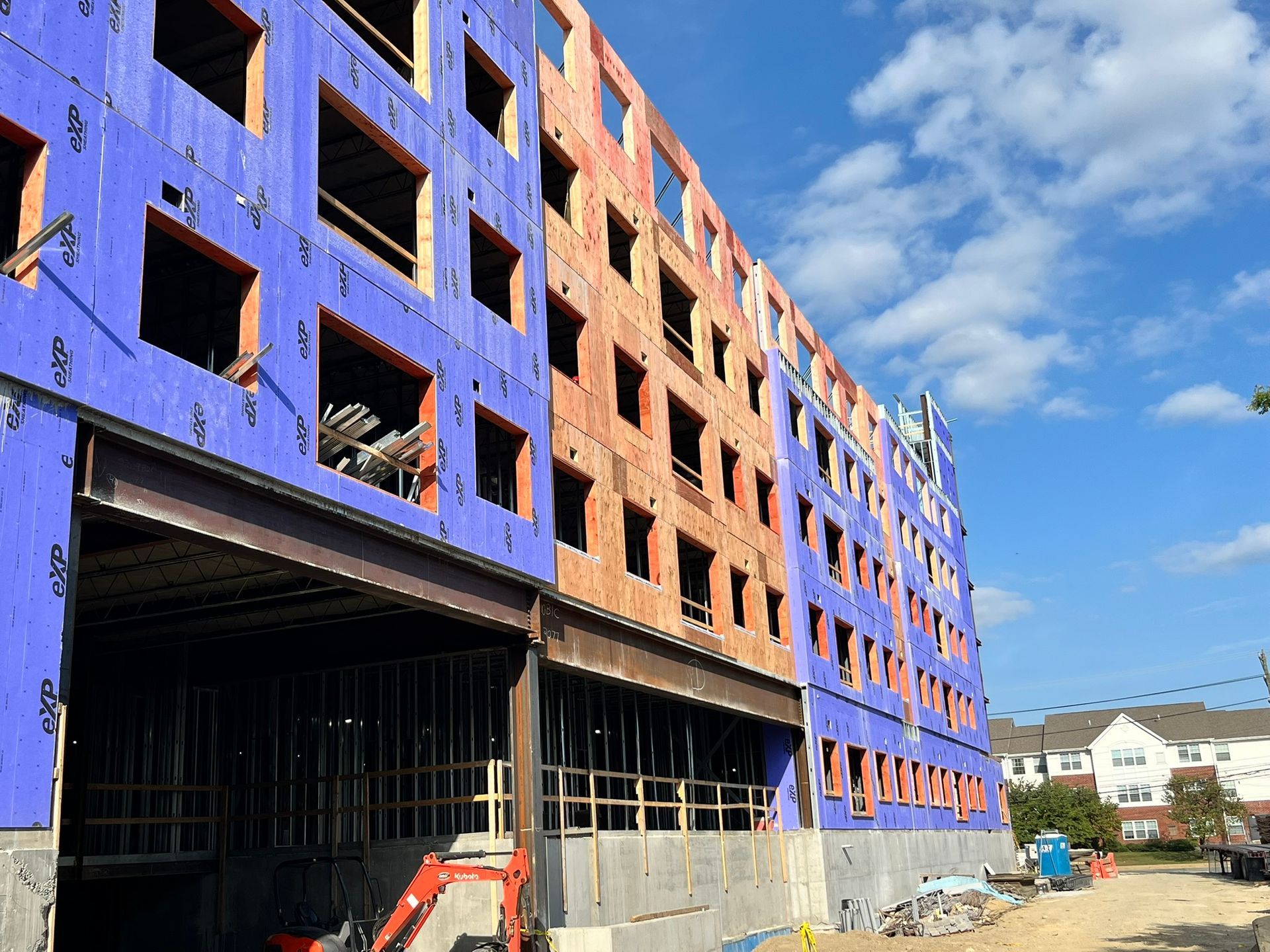 Partially built apartment building with blue and orange exterior panels and construction equipment below.
