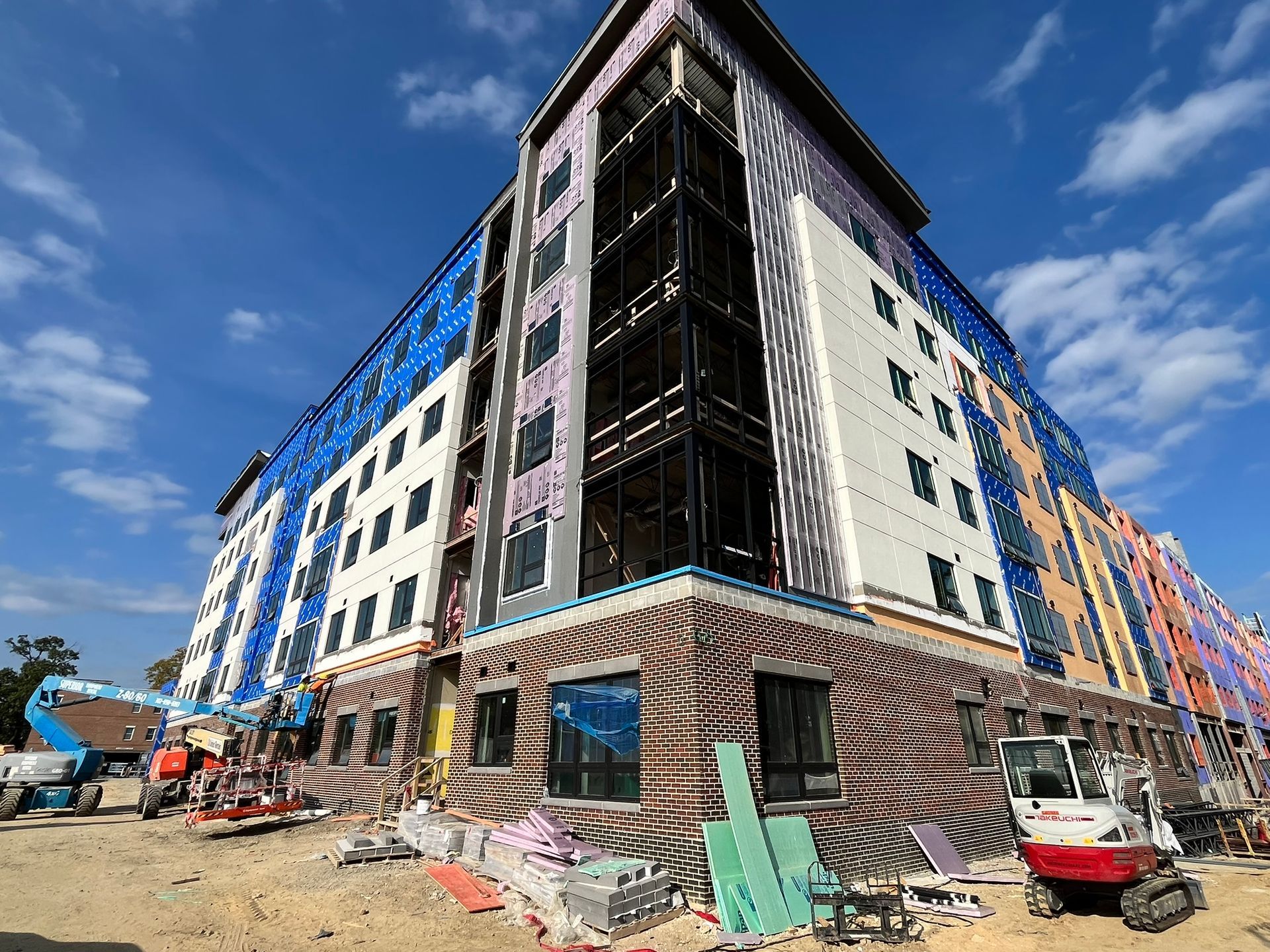 Street-level view of a multistory building under construction with scaffolding and debris under a blue sky.