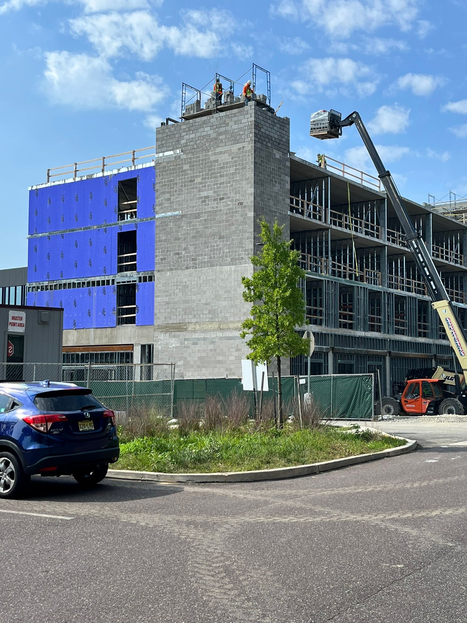 Partially built multi-story building with blue panels, scaffolding, and construction equipment under a clear sky.