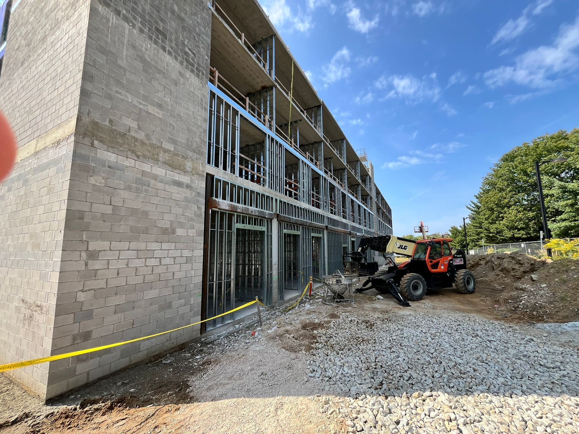 Construction site beside an apartment building with scaffolding, gravel, caution tape, and a small loader.