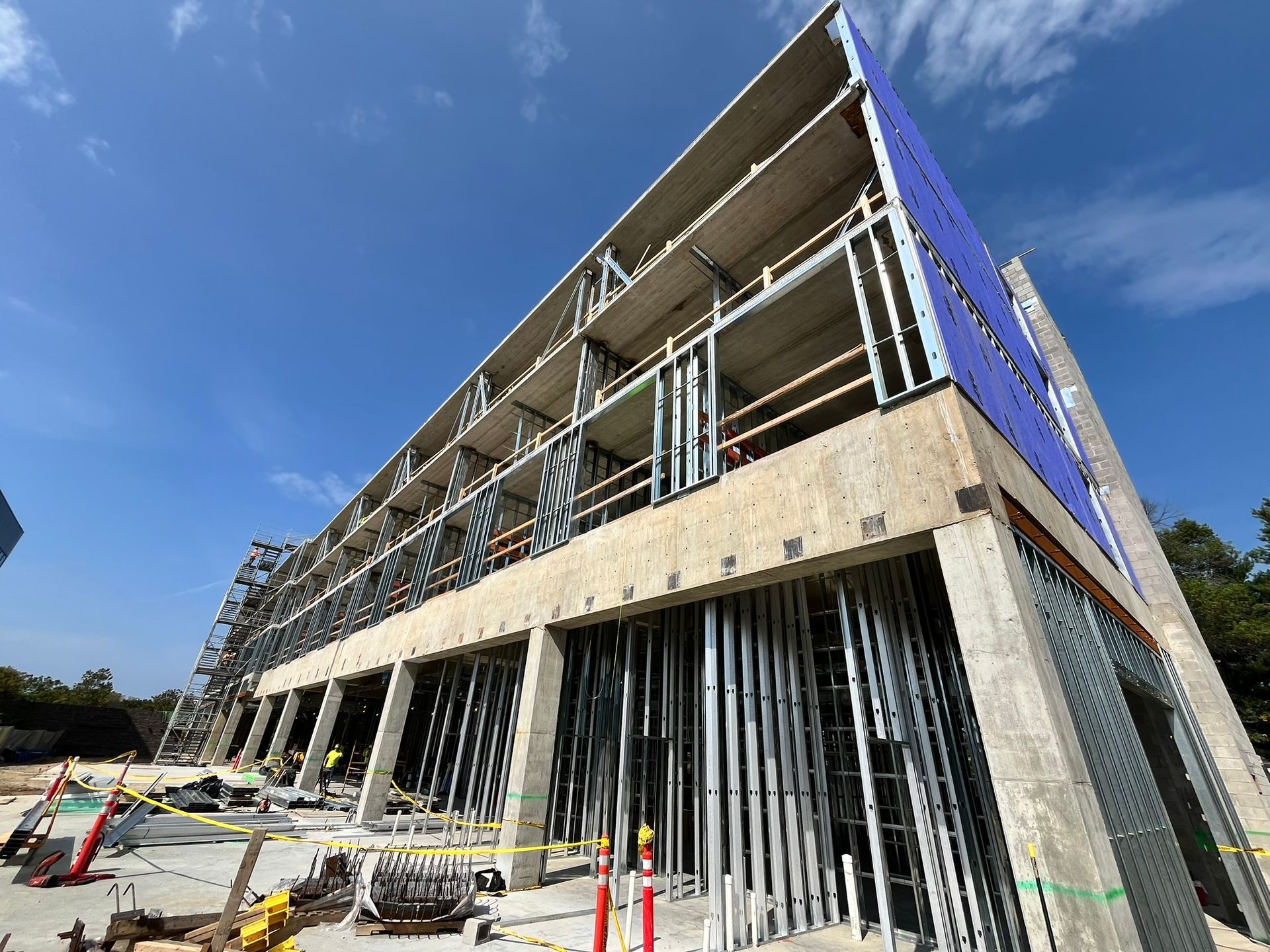 Modern building under construction with exposed concrete, metal framing, and blue sky